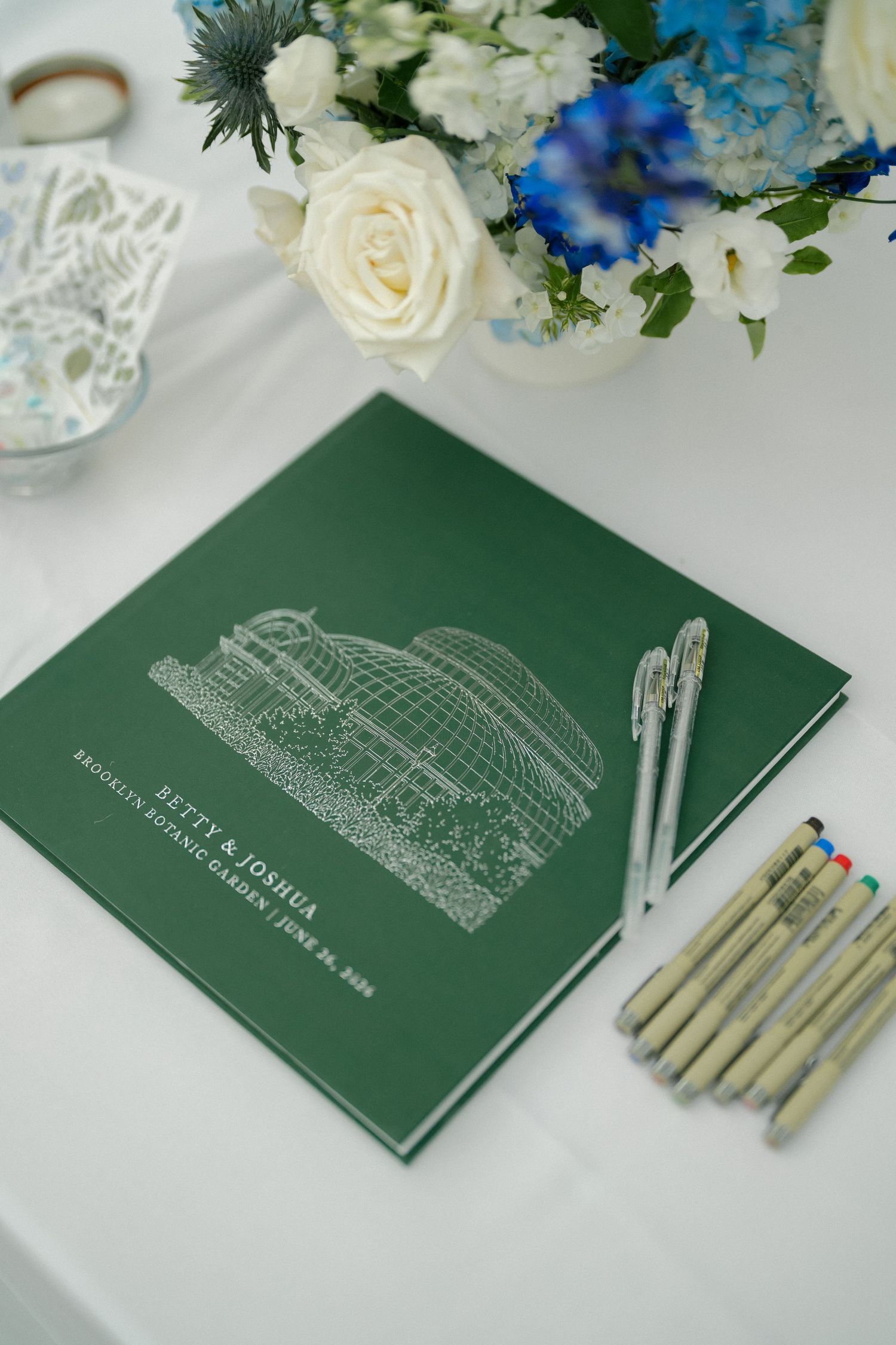 Green wedding guest book for Betty and Joshua at Brooklyn Botanic Garden with pens and floral arrangement.