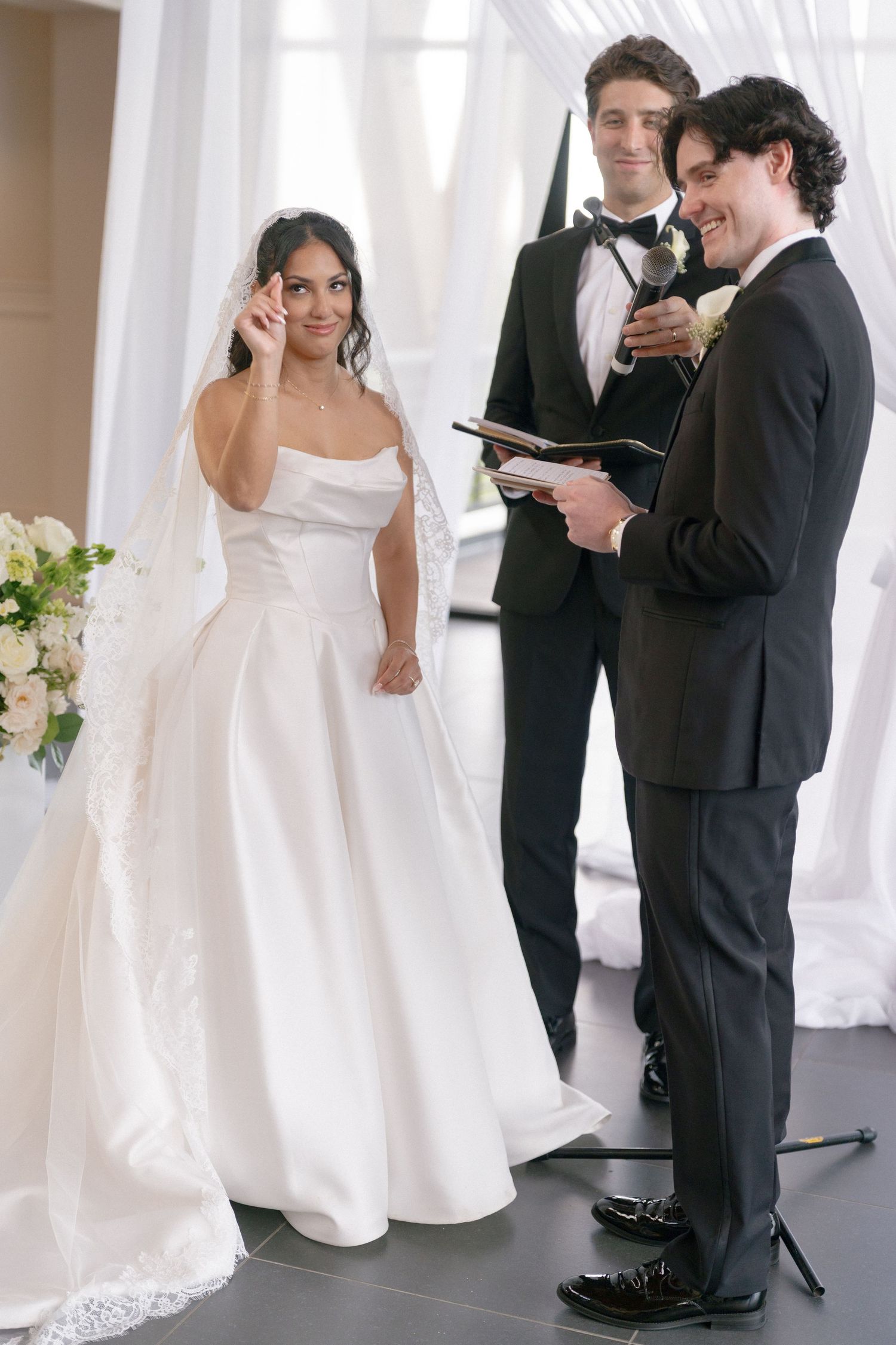 Bride wiping tears while groom reads vows during elegant indoor wedding ceremony with officiant.