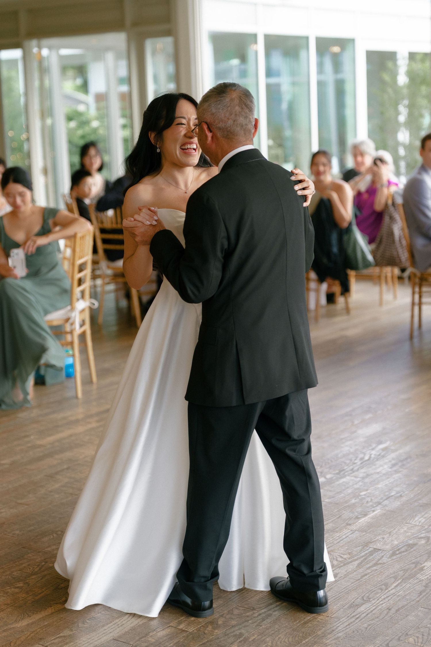 Bride in white strapless gown laughs joyfully while sharing a dance with a guest at wedding reception.