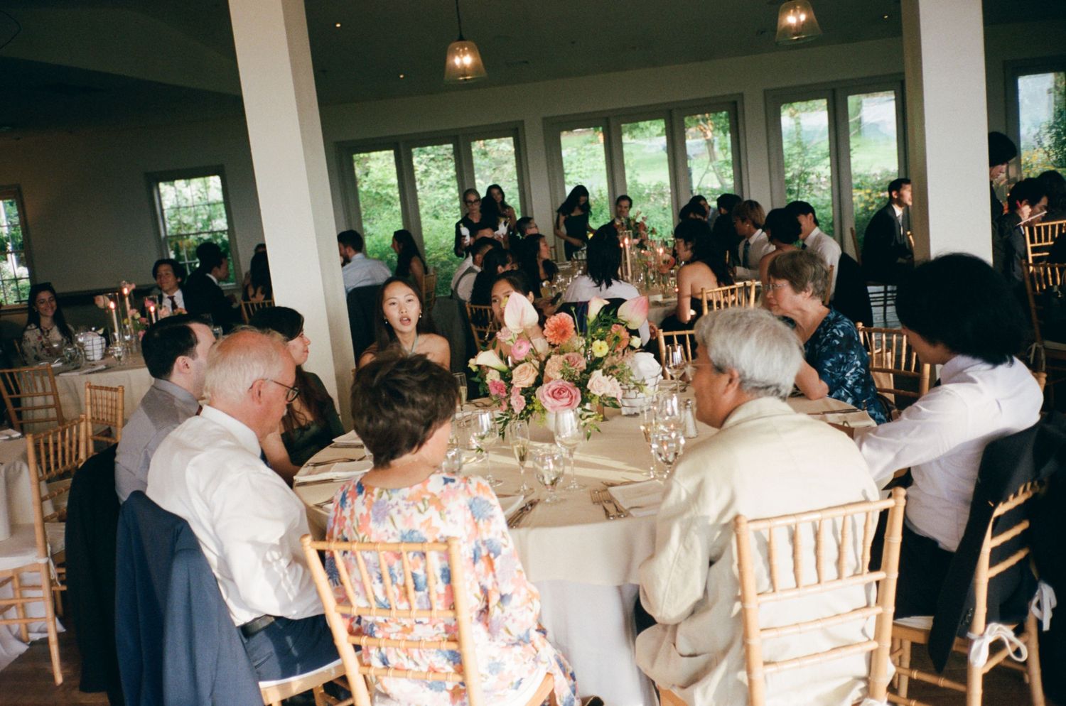Wedding reception guests seated at round tables with floral centerpieces in elegant venue.