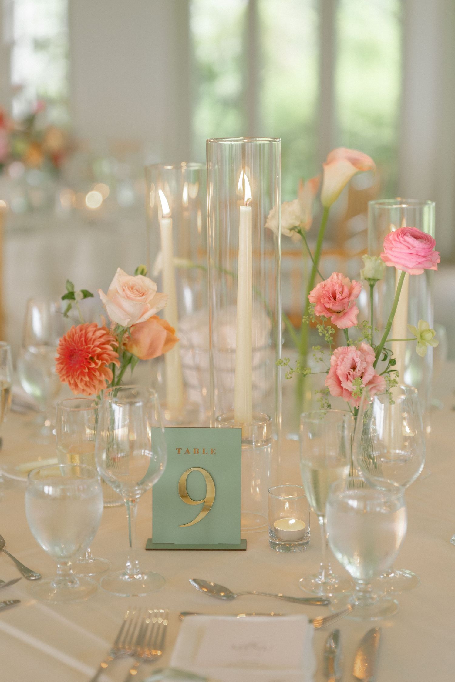 Elegant wedding table centerpiece with candles, coral and pink flowers, and a mint green Table 9 card.