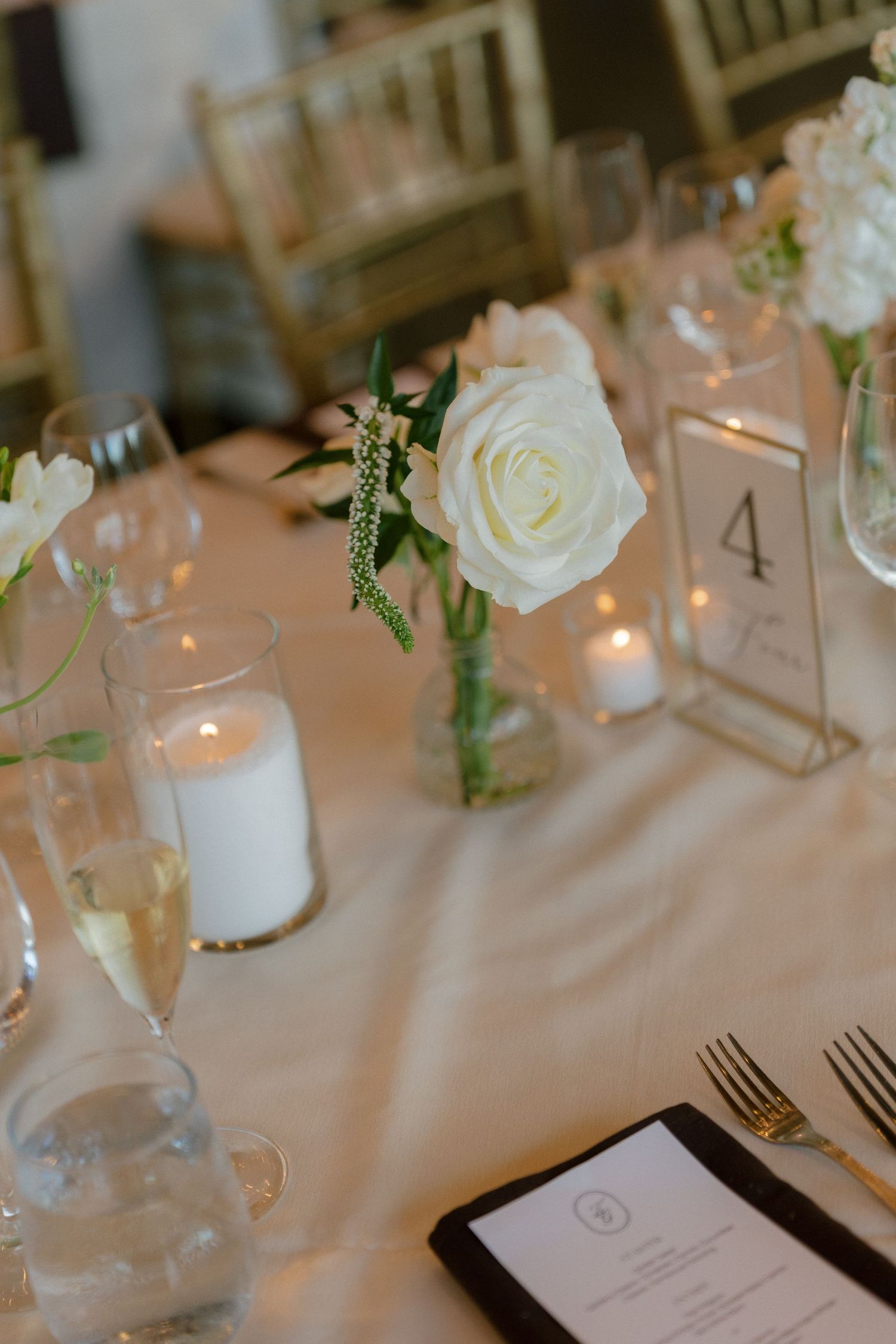 Elegant wedding reception table with white roses, candles, and table number four centerpiece.