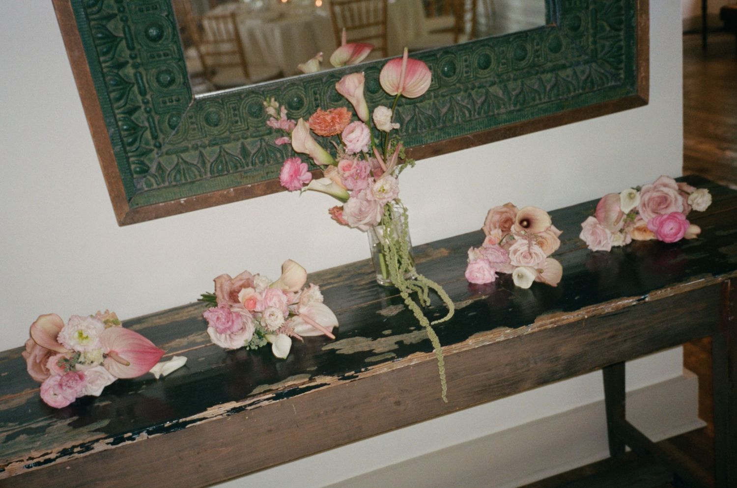 Pink and blush floral arrangements with orchids and ranunculus displayed on a rustic wooden bench.
