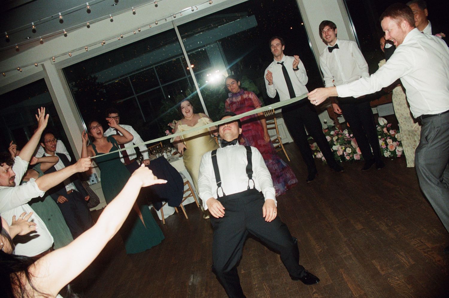 Energetic wedding guest does limbo dance move on reception dance floor surrounded by cheering crowd.