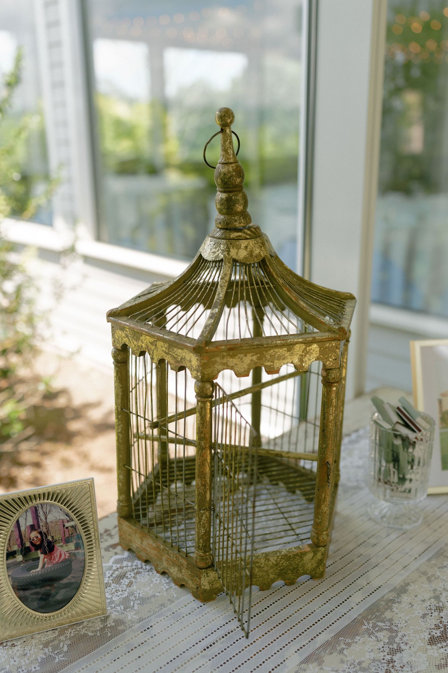 Ornate antique gold birdcage decoration on lace tablecloth at elegant wedding reception venue.