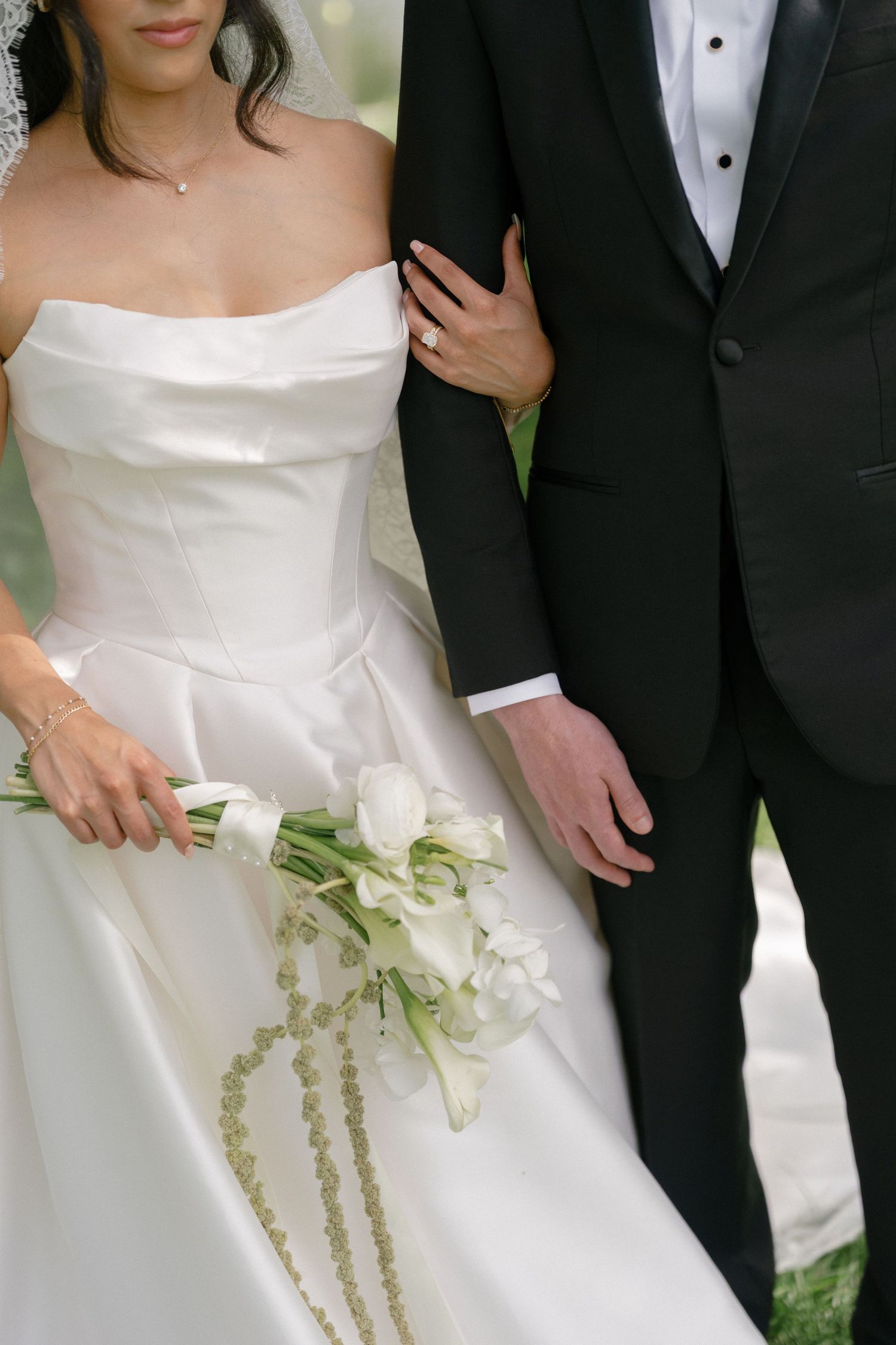 Bride in strapless white gown holding white tulip bouquet stands beside groom in black tuxedo at wedding.