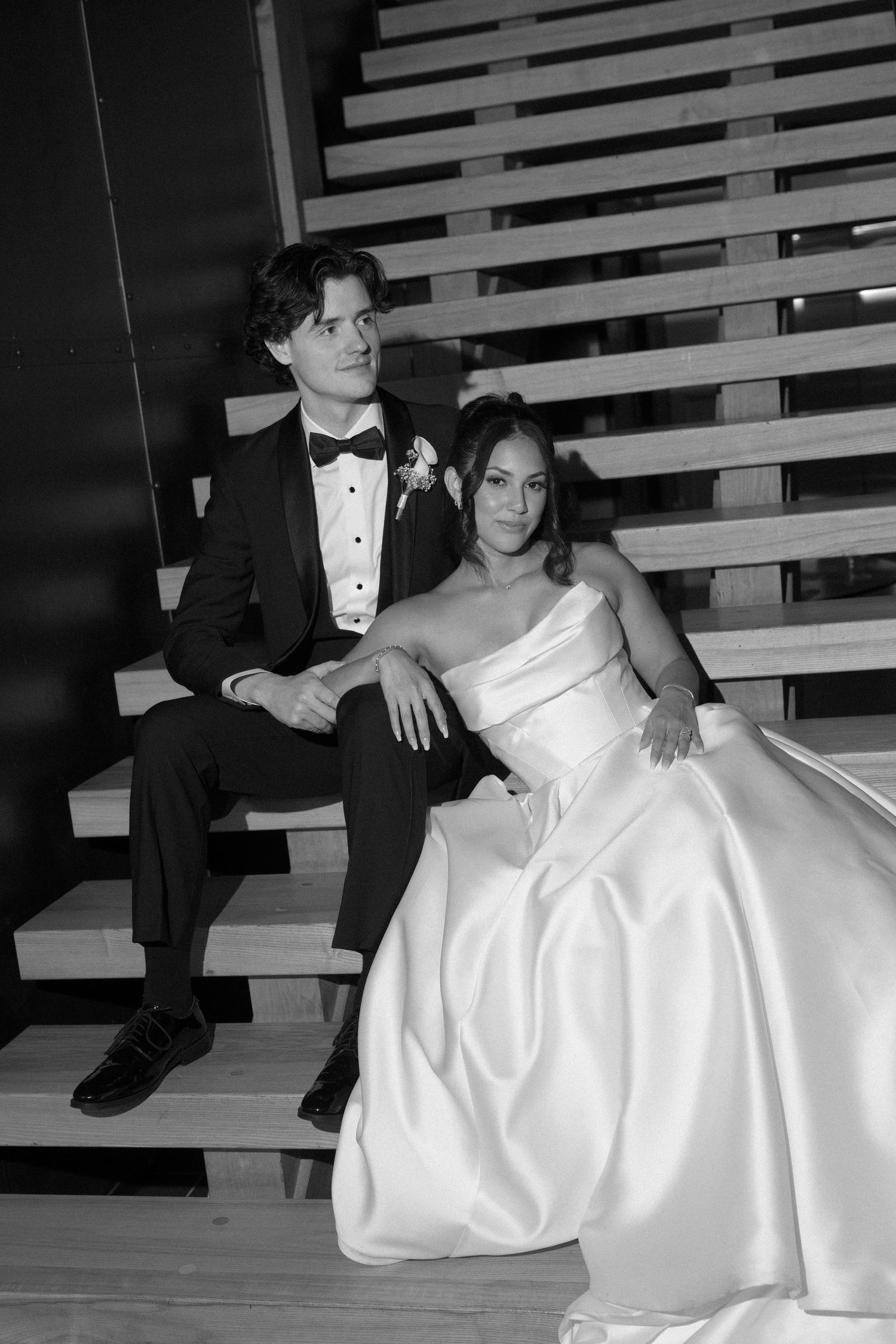 Black and white portrait of bride and groom sitting together on wooden stairs.
