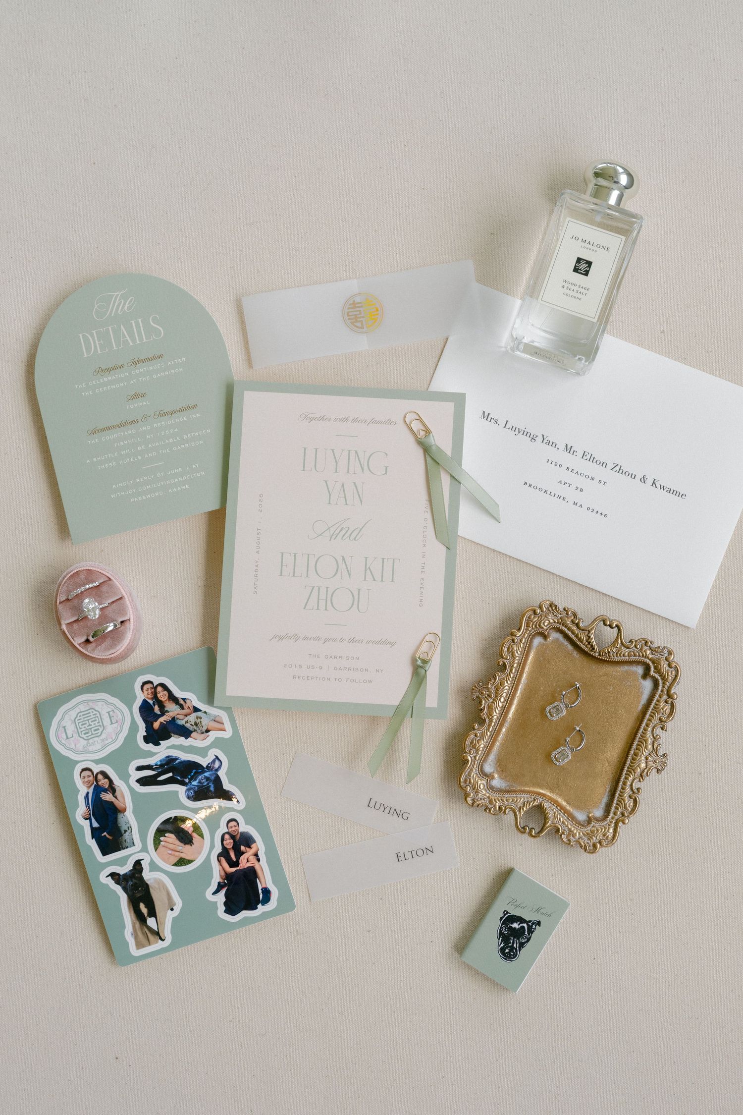 Elegant wedding flat lay with sage green invitations, diamond rings, custom stickers, and Jo Malone perfume on neutral background.