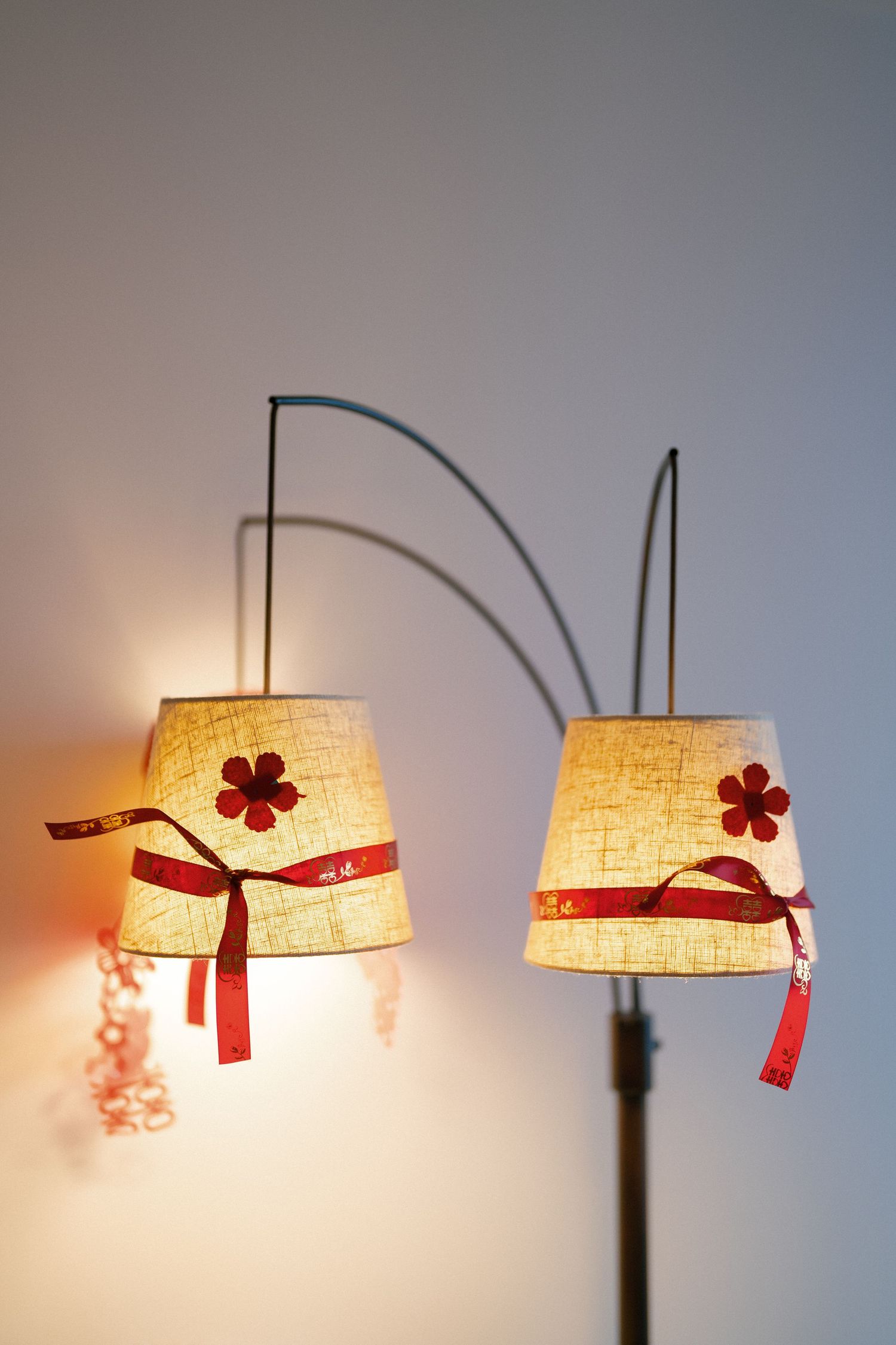 Decorative dual arc floor lamp with burlap shades adorned with red ribbon bows and floral accents.