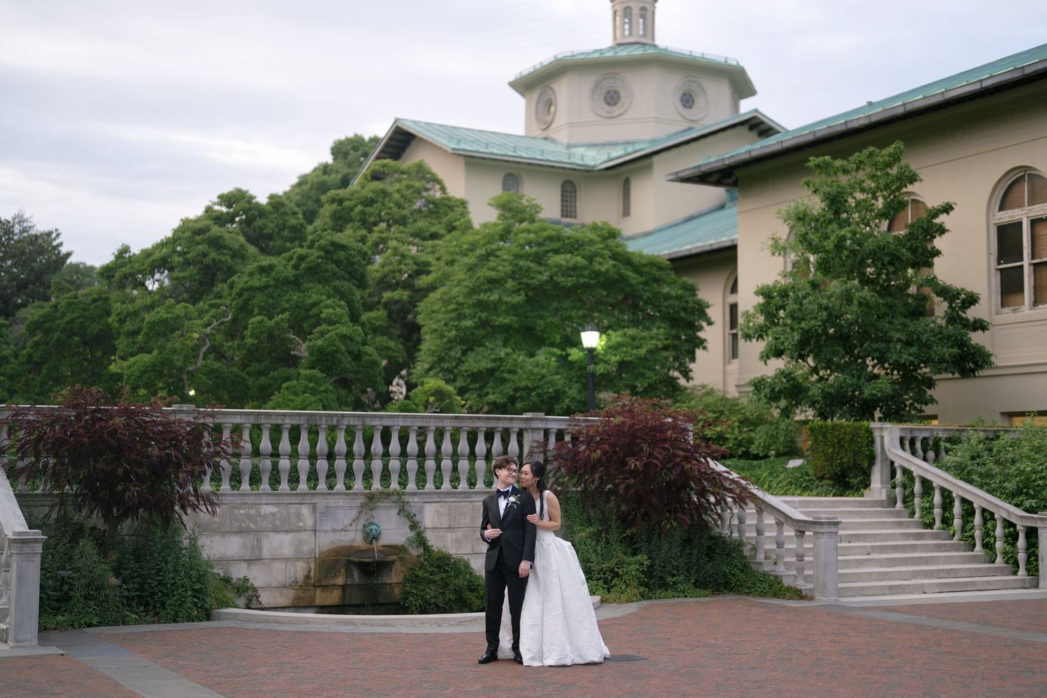 Bride and groom embrace near ornate balustrade and domed venue.
