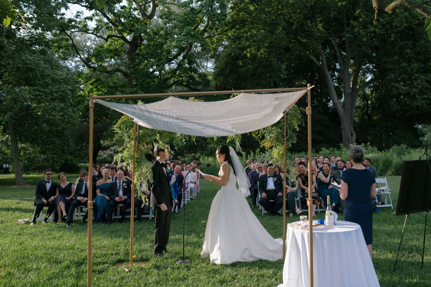 Bride and groom exchange vows under a floral chuppah during an elegant outdoor Jewish wedding ceremony.
