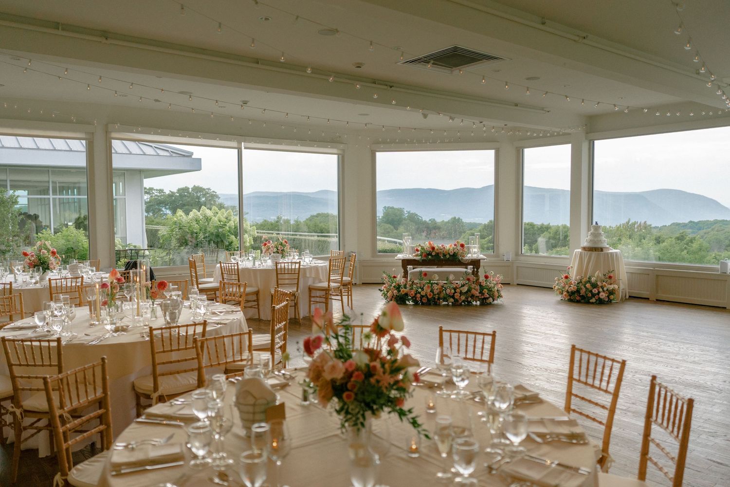 Elegant wedding reception hall with panoramic mountain views, gold Chiavari chairs, and floral centerpieces.