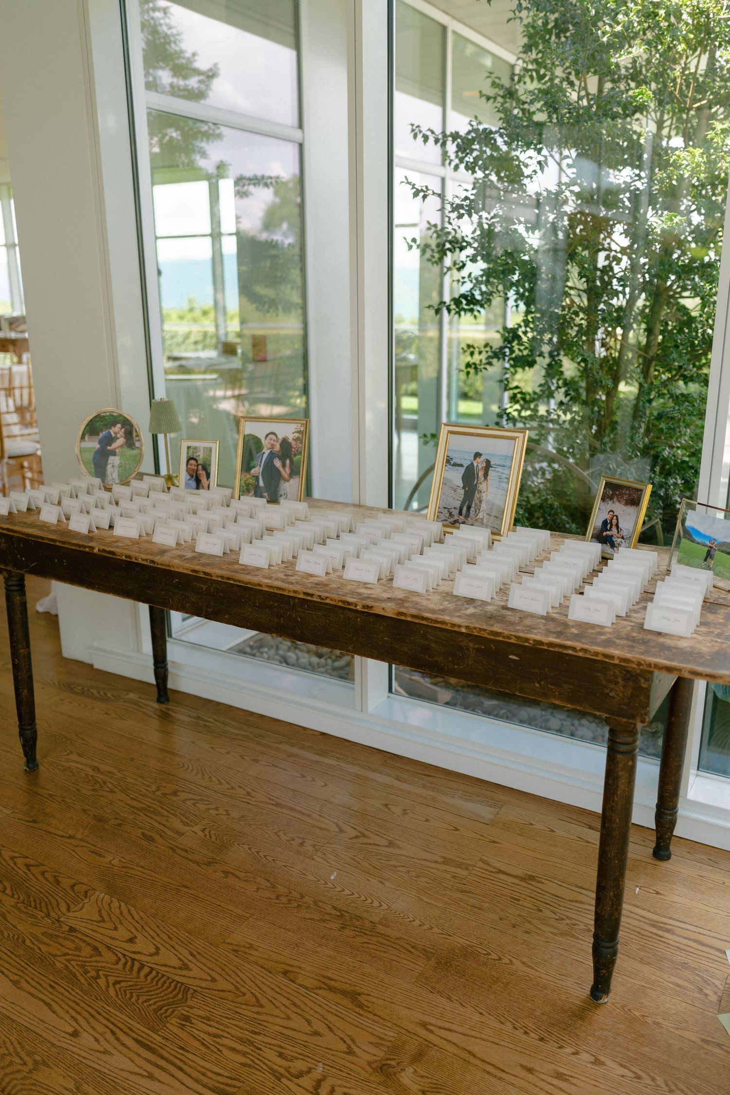 Rustic wooden escort card table with framed photos and white place cards at an elegant wedding reception.