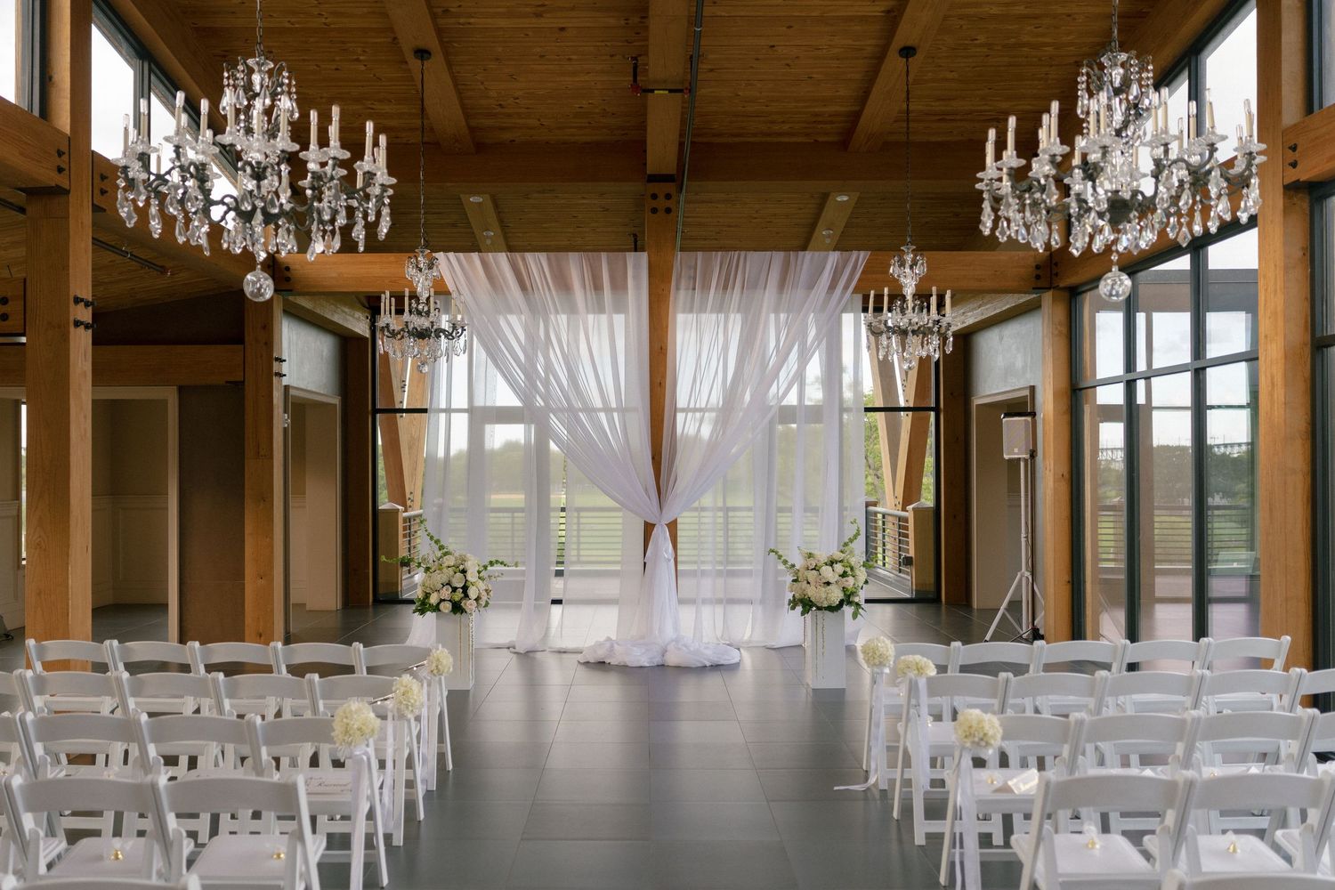 Elegant wedding ceremony venue with crystal chandeliers, white chairs, and draped floral arch.