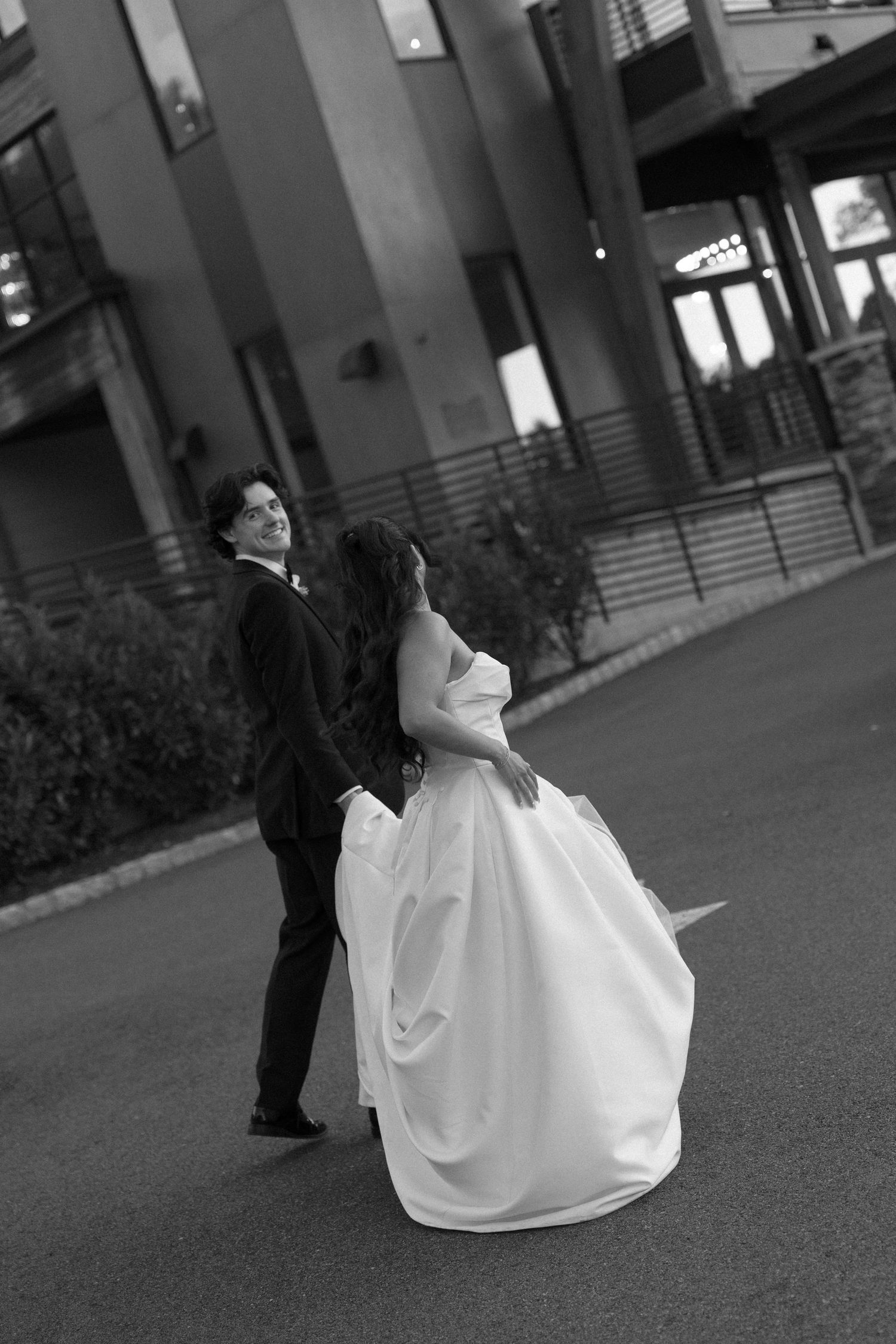 Black and white photo of bride and groom sharing romantic moment on street outside elegant building at dusk.