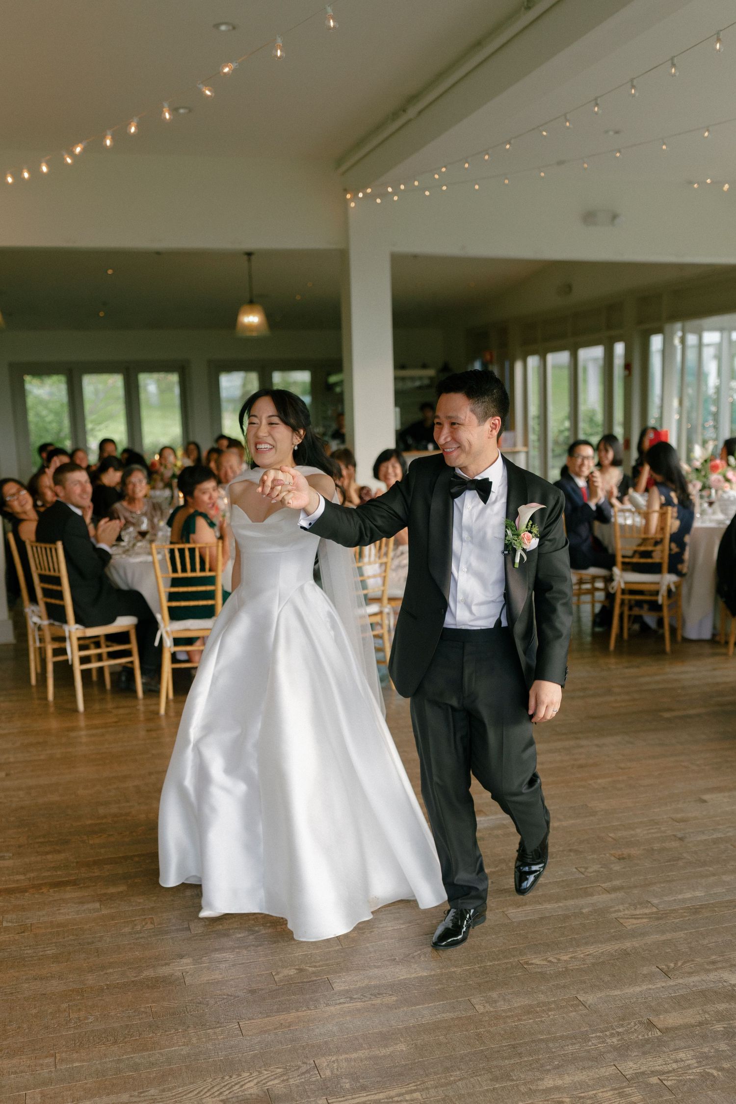 Bride and groom make grand entrance onto dance floor at elegant indoor wedding reception.