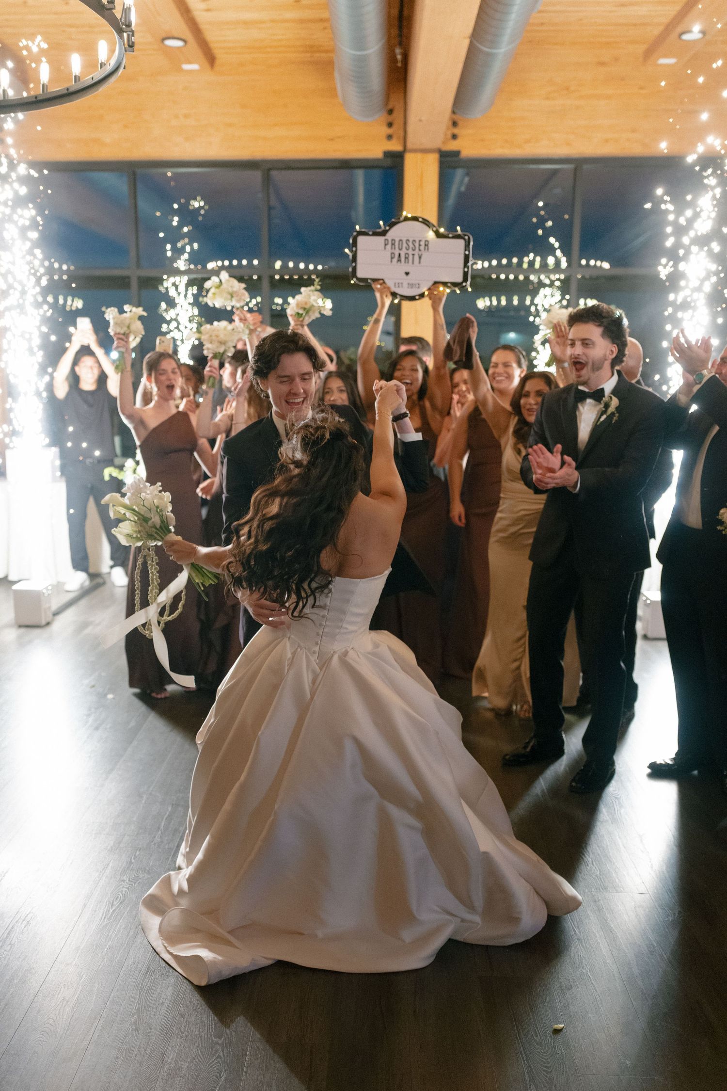 Bride and groom celebrate first dance surrounded by sparklers and cheering wedding guests.