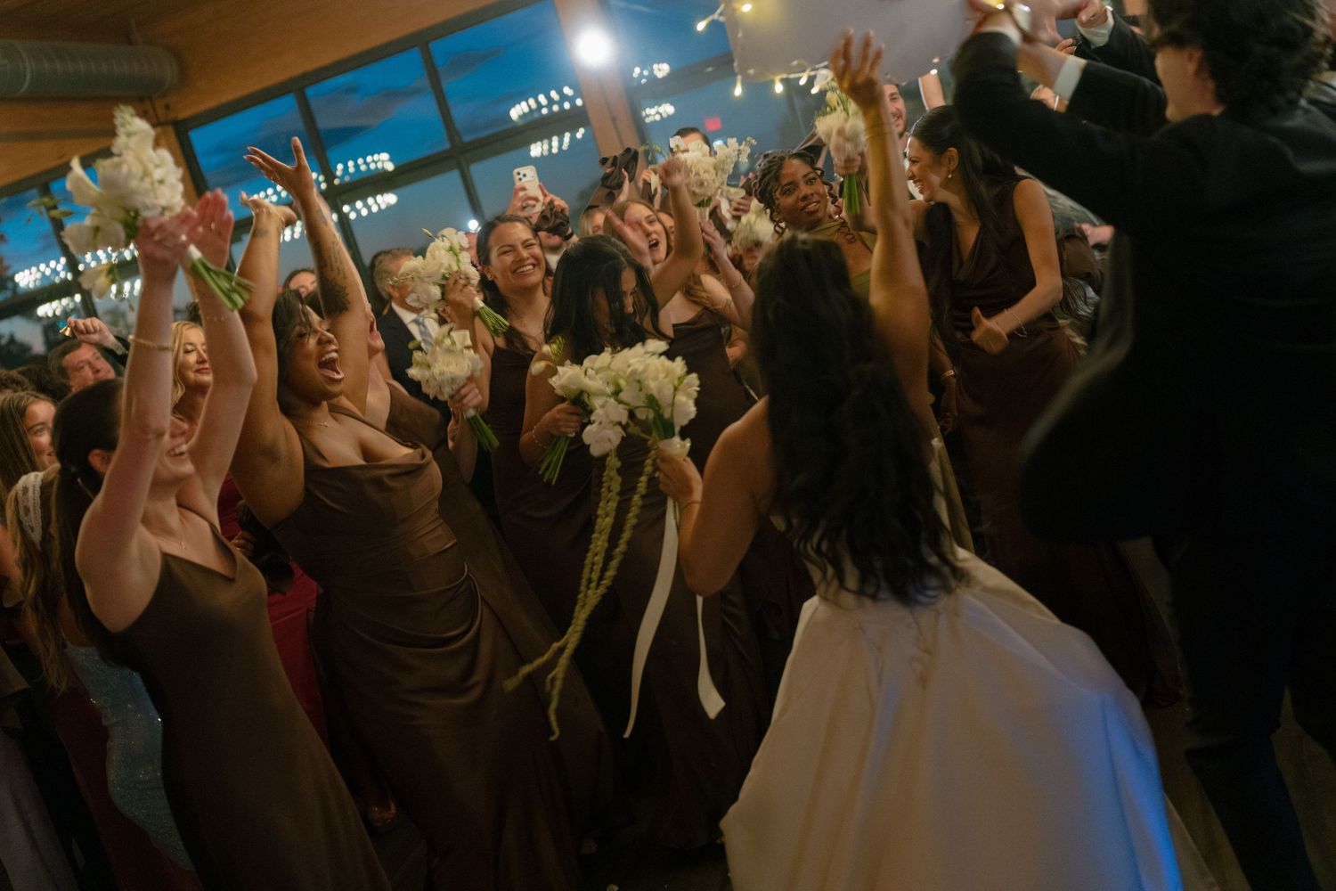 Bride tossing bouquet to excited guests at indoor wedding reception celebration.