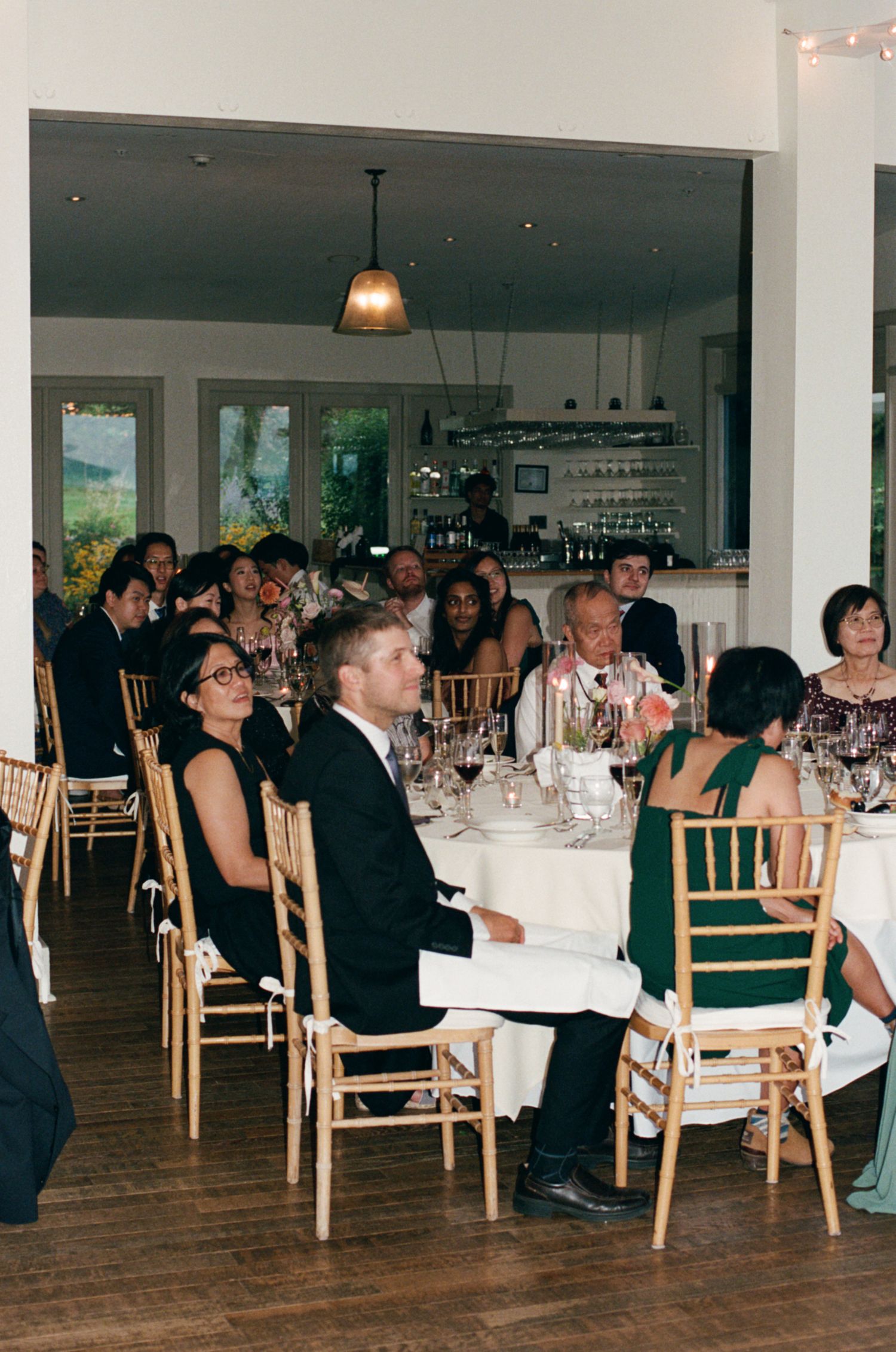 Wedding guests in formal attire seated at elegantly set round tables during indoor reception dinner.