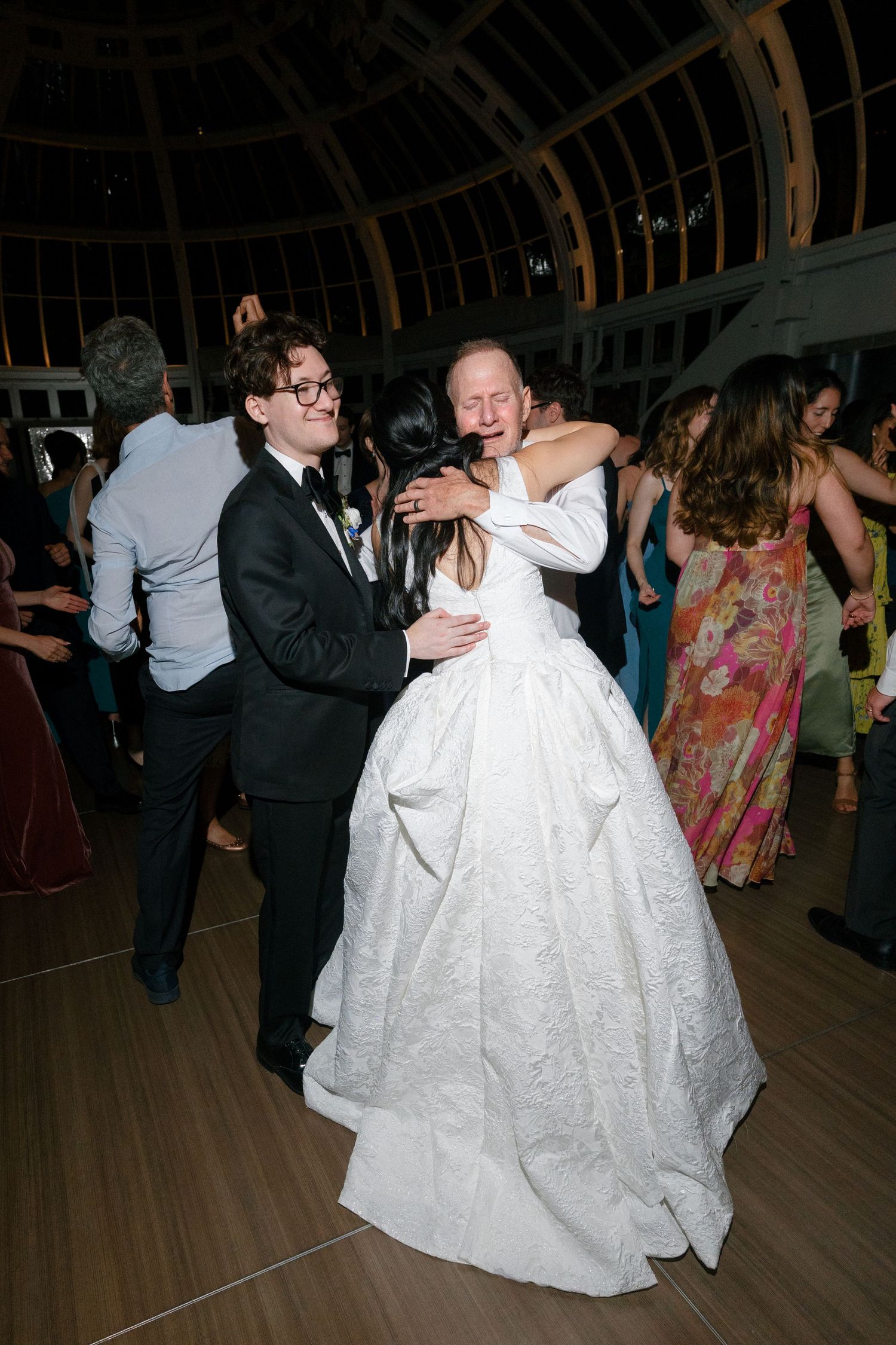 Bride in voluminous white gown dances joyfully with groom in tuxedo at elegant wedding reception.