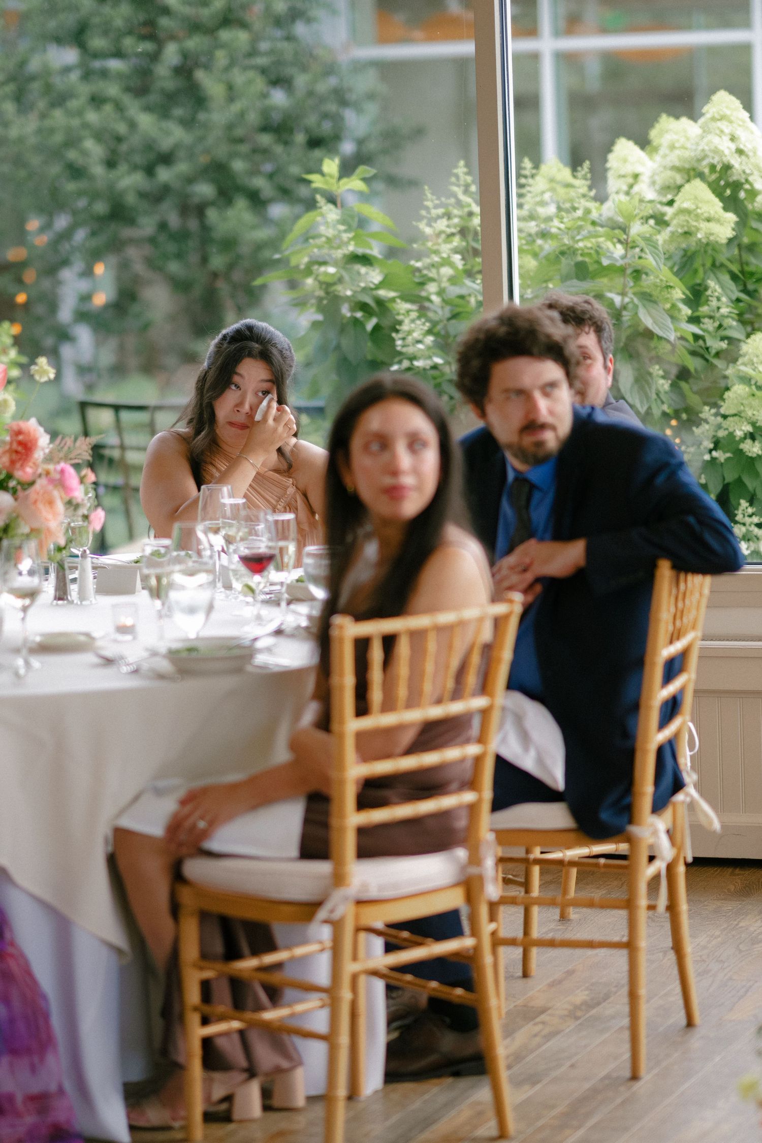 Wedding guests seated at elegantly decorated reception table with lush greenery backdrop.
