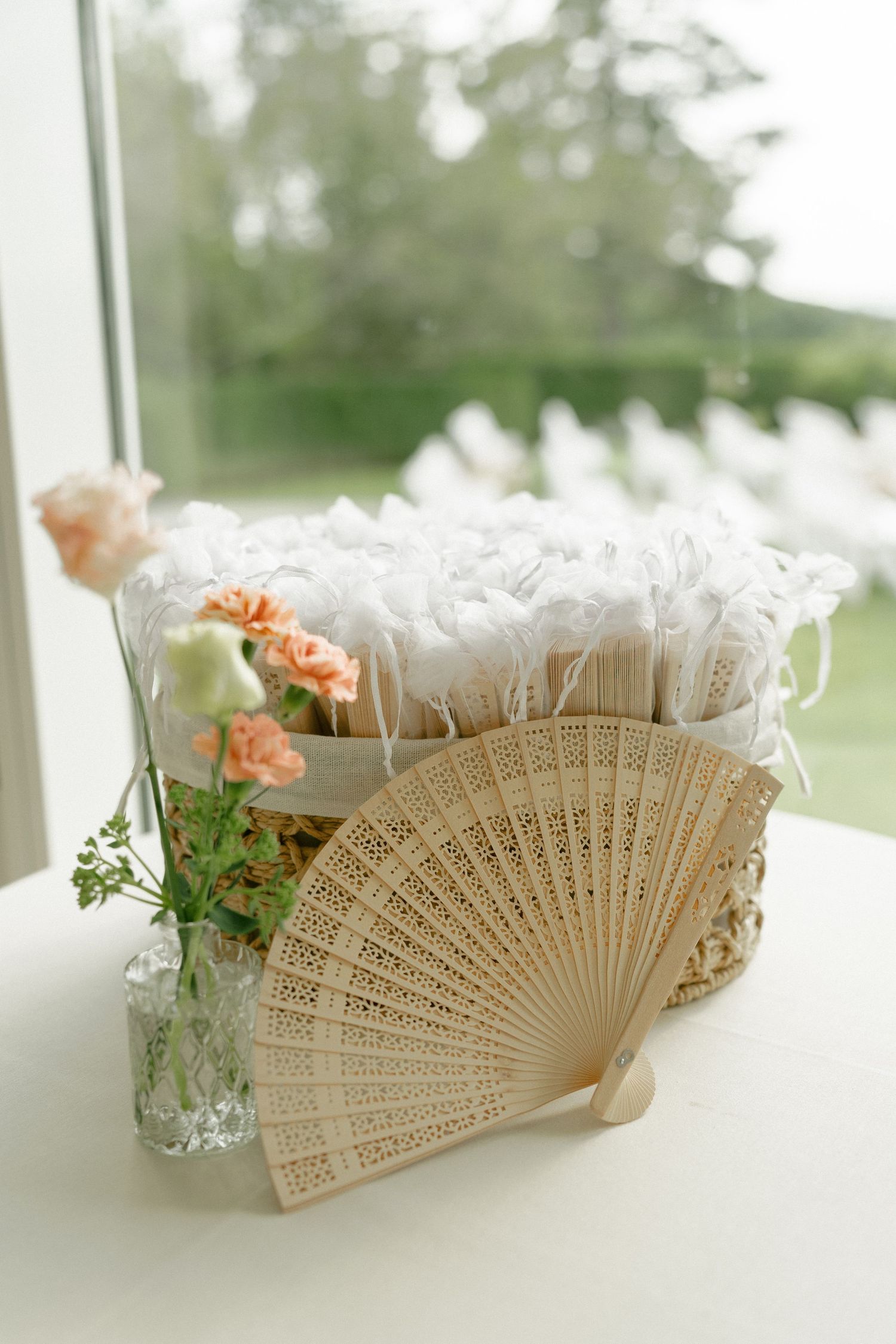 Wooden hand fan display with white lace fans in basket and peach roses in glass vase.
