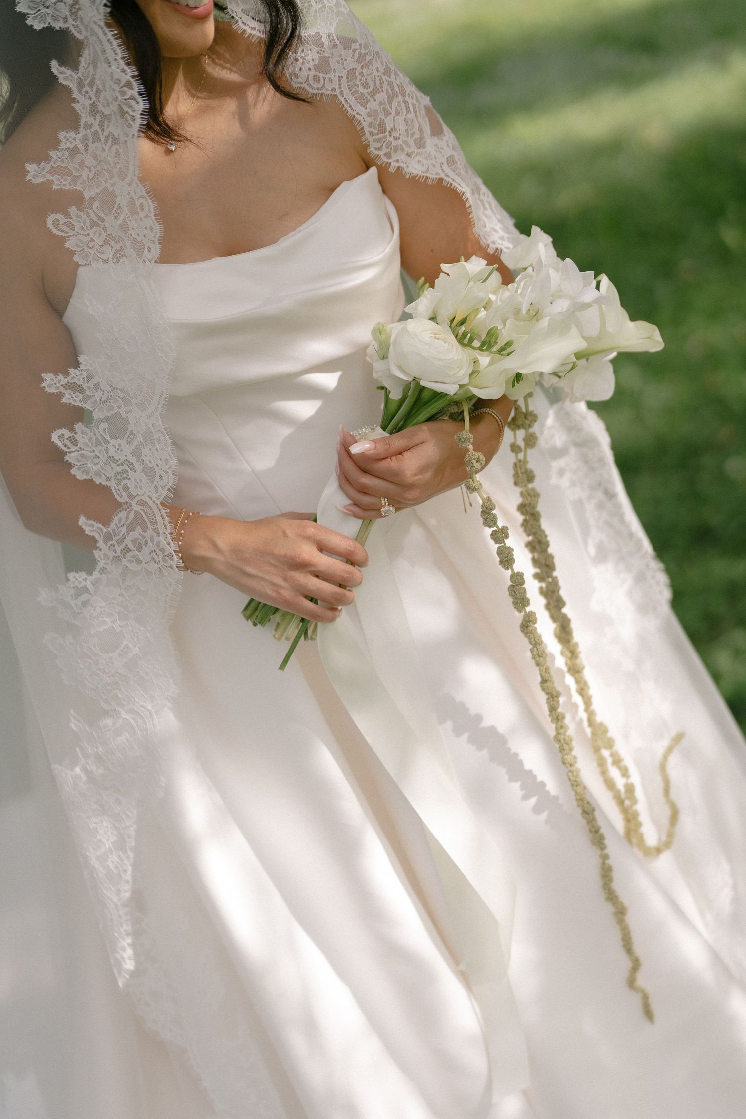 Bride in white ball gown holds elegant bouquet of white flowers with gold pearl accents outdoors.