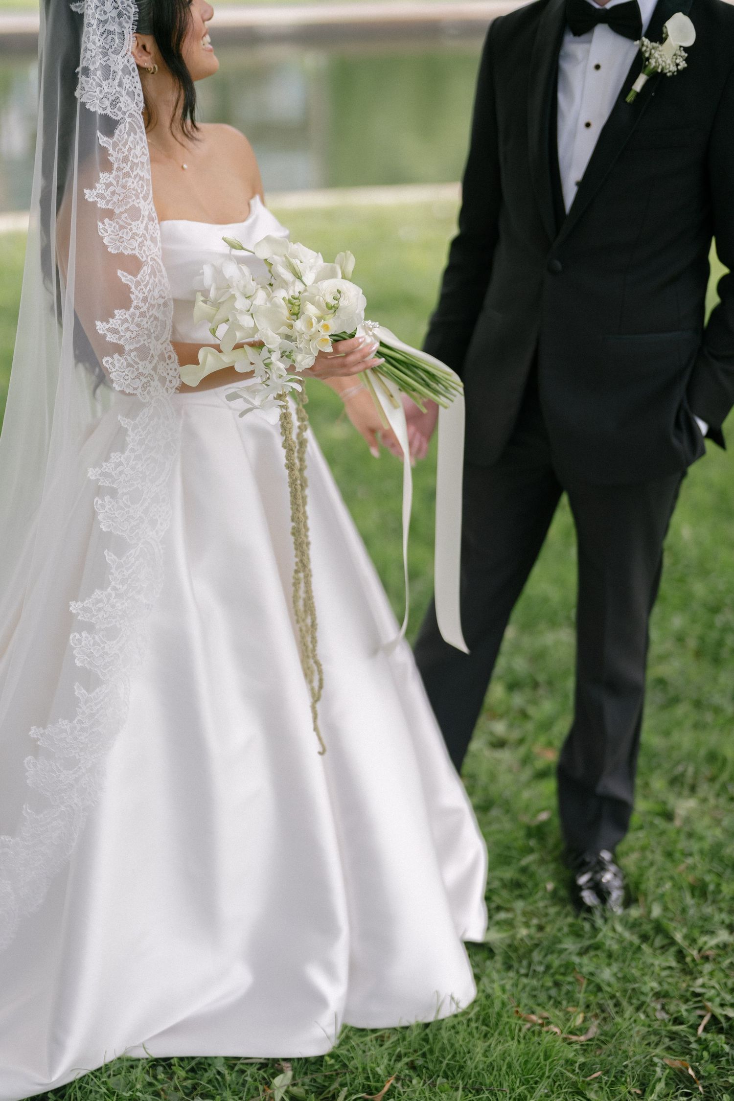 Bride in strapless satin ballgown with lace veil holds white orchid bouquet beside groom in black tuxedo.
