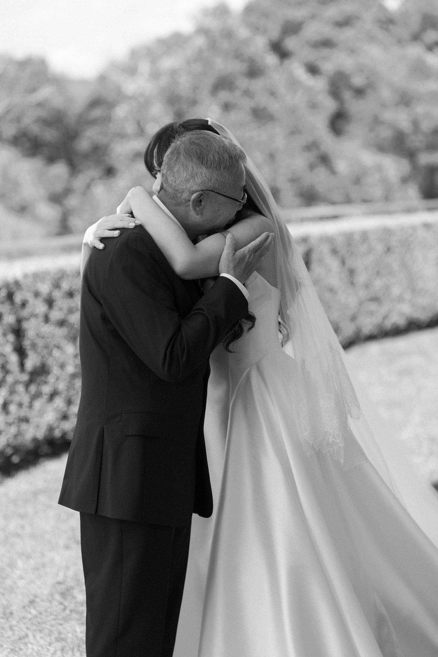 Emotional black and white photo of bride and father embracing outdoors before wedding ceremony.
