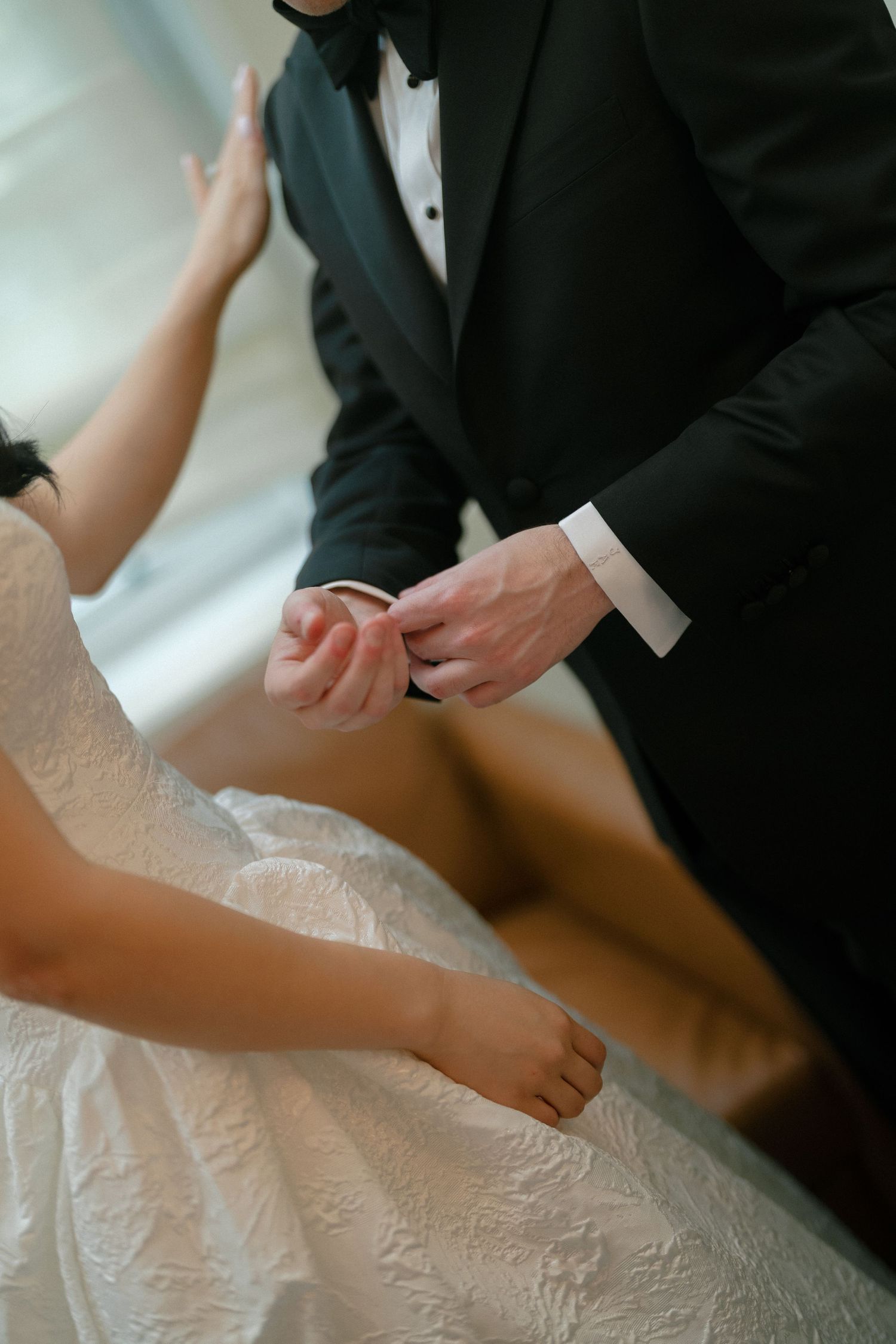 Groom in black tuxedo placing a wedding ring on bride's finger during ceremony.