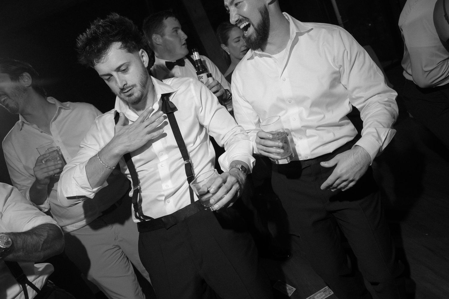 Black and white photo of two men in white shirts dancing and laughing at a wedding reception.