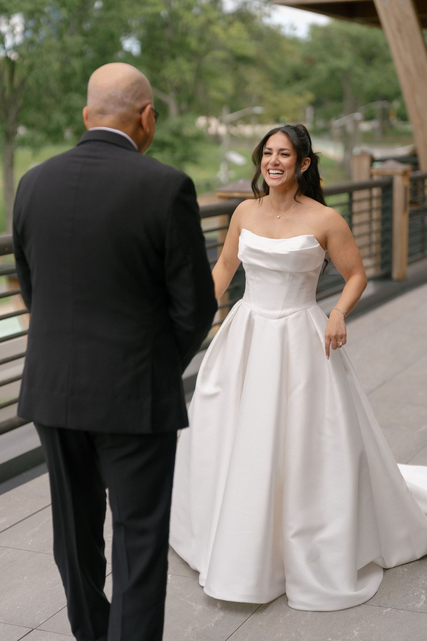 Bride in strapless white ballgown laughing during first look with groom in black suit outdoors.