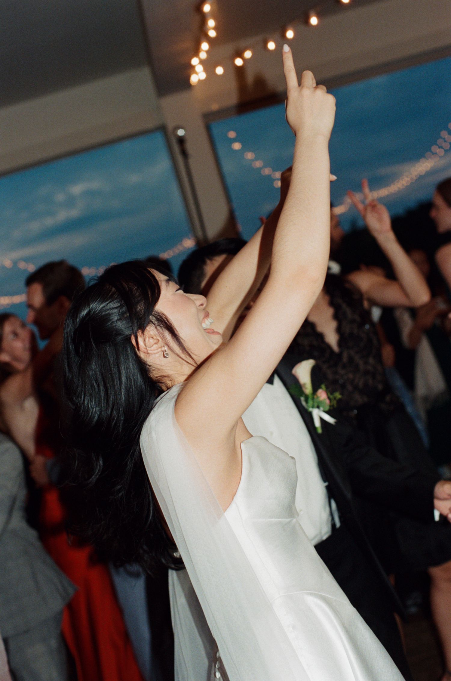 Bride in white wedding dress dancing joyfully with arm raised at elegant wedding reception.
