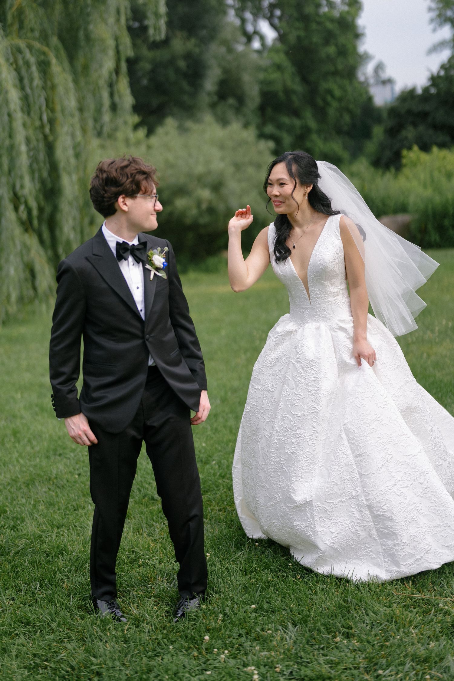 Bride in white ball gown and groom laugh on green lawn.