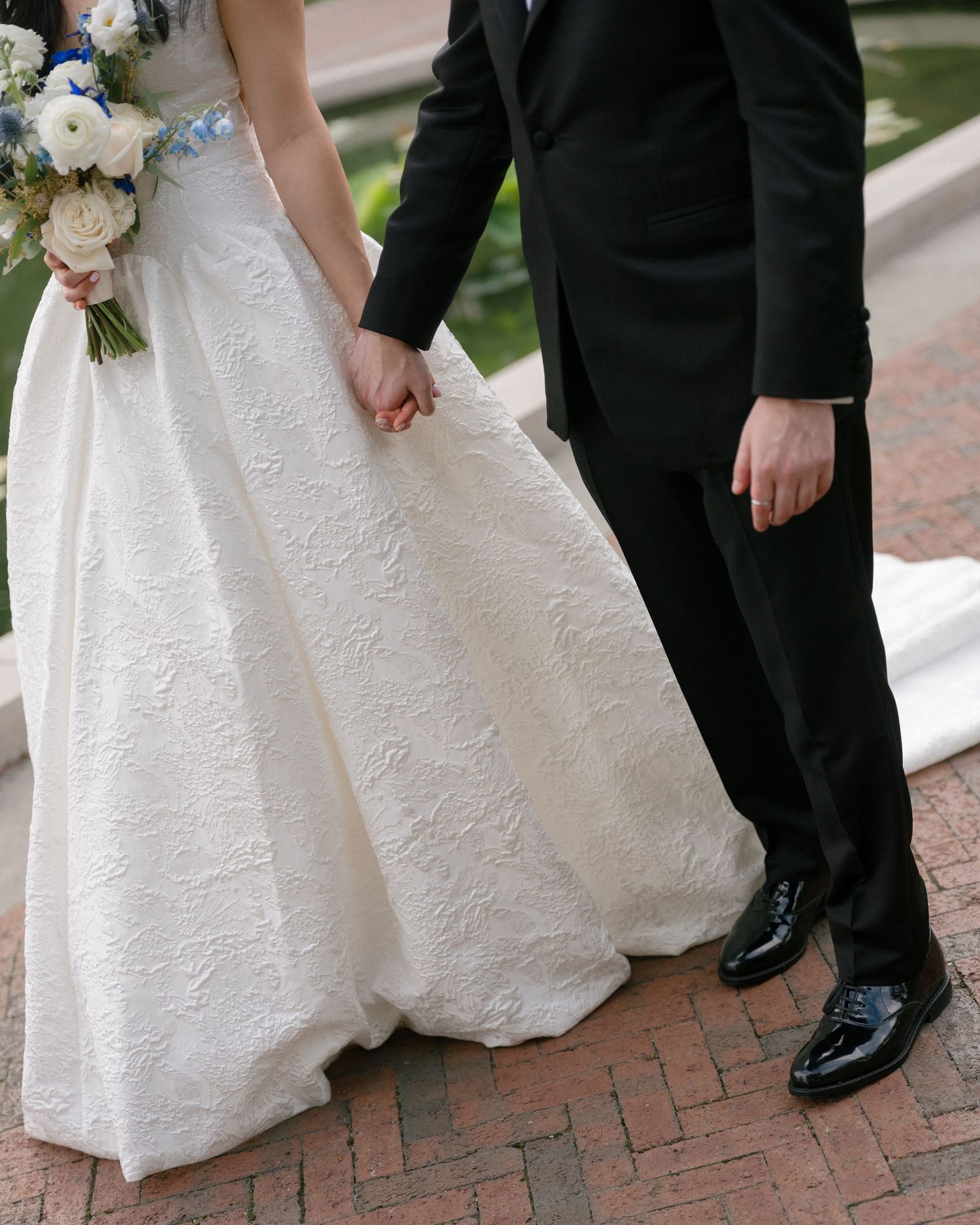 Bride in white lace ball gown holding a bouquet and groom in black suit holding hands at their wedding.
