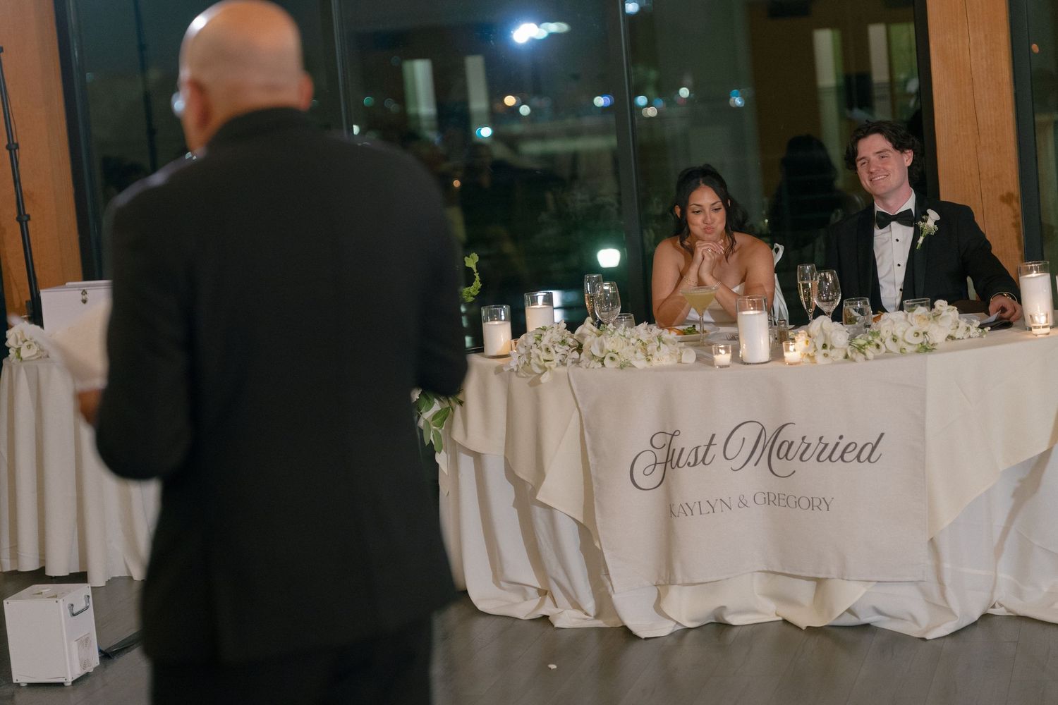 Couple at sweetheart table with Just Married banner during wedding reception speech.