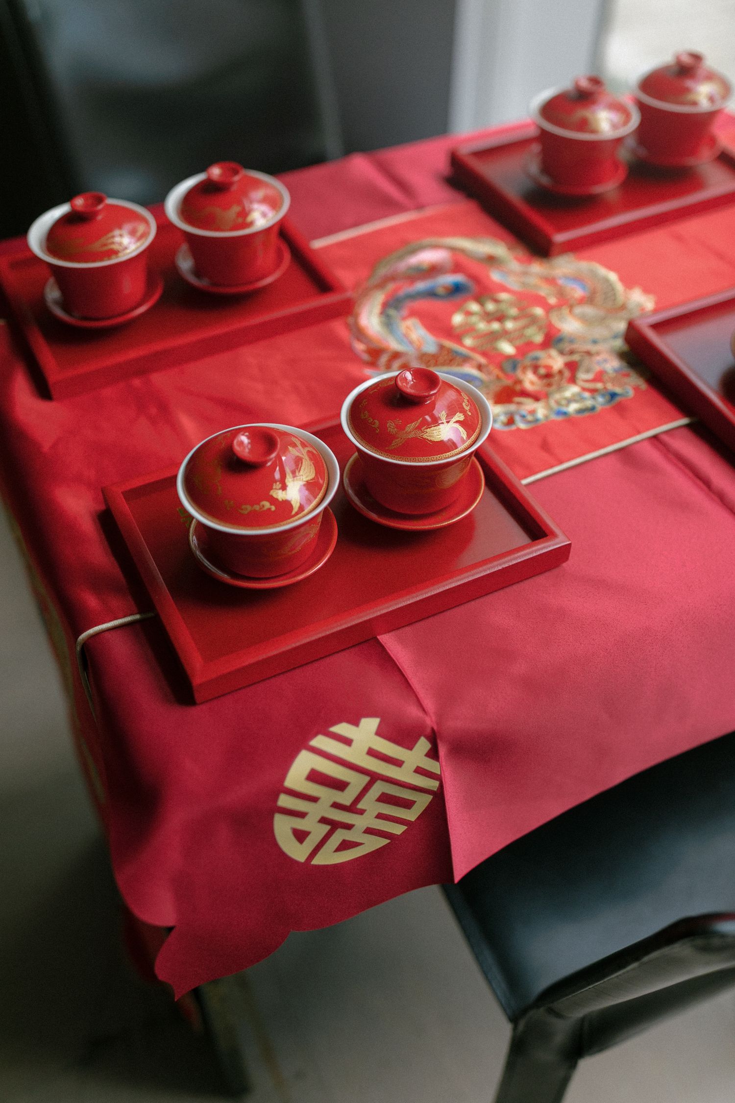 Red Chinese wedding tea ceremony set with lidded cups on red trays, double happiness symbol on tablecloth.