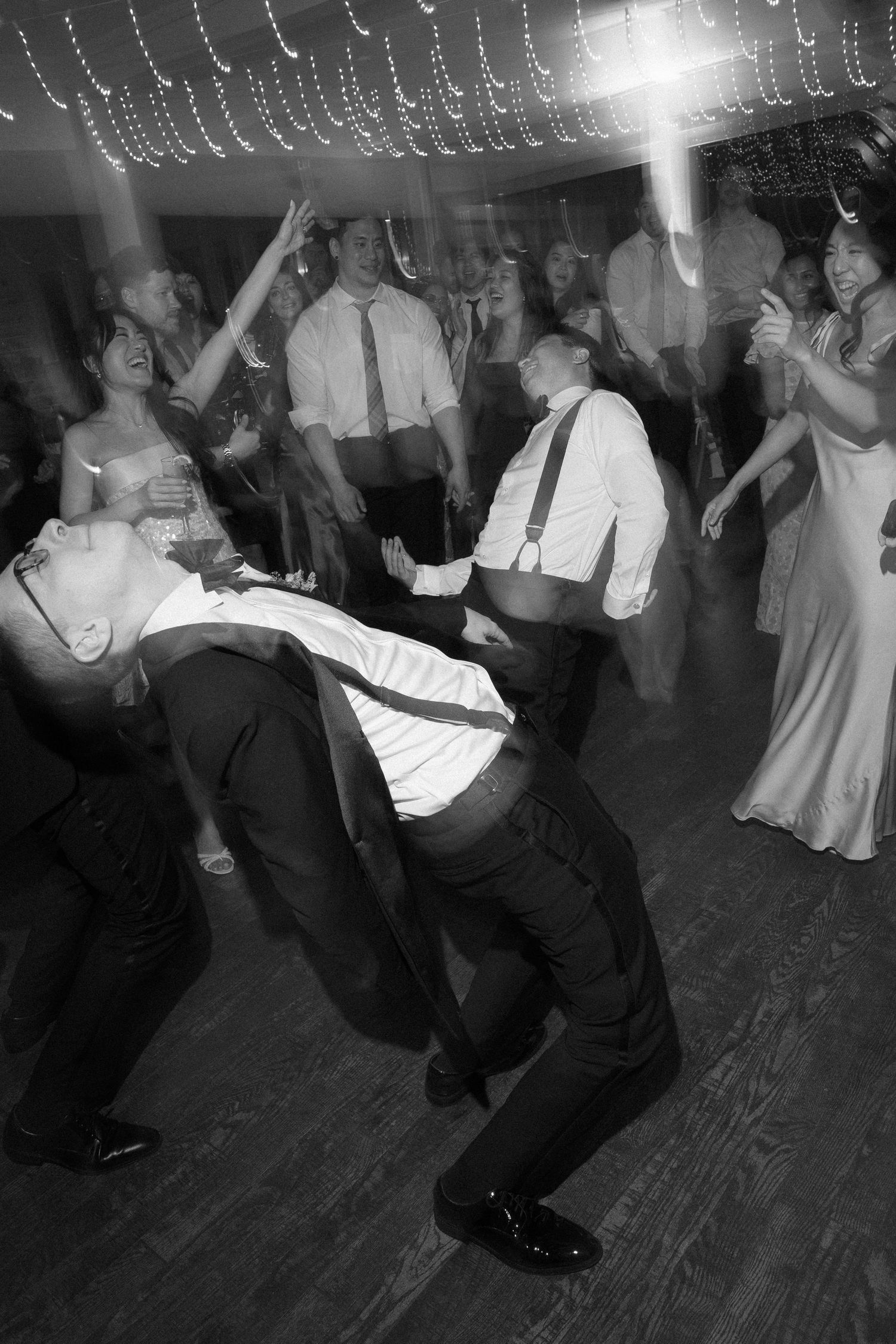 Energetic black and white photo of wedding guests dancing wildly at lively reception.