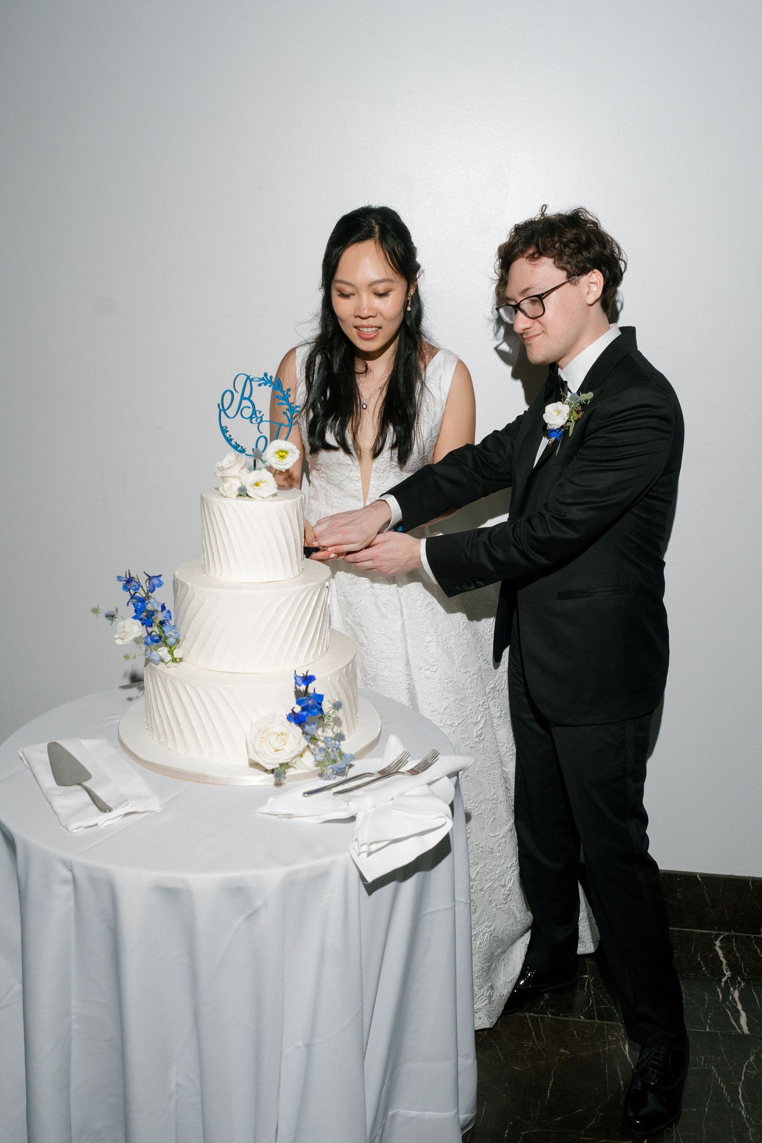Bride and groom cut white tiered wedding cake at reception.
