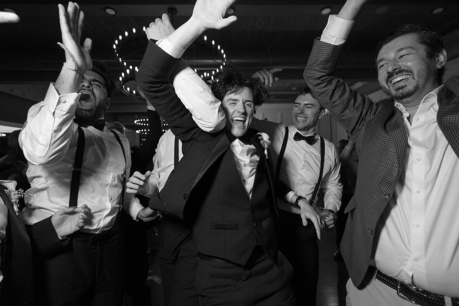 Black and white photo of joyful groomsmen dancing and celebrating at a wedding reception party.