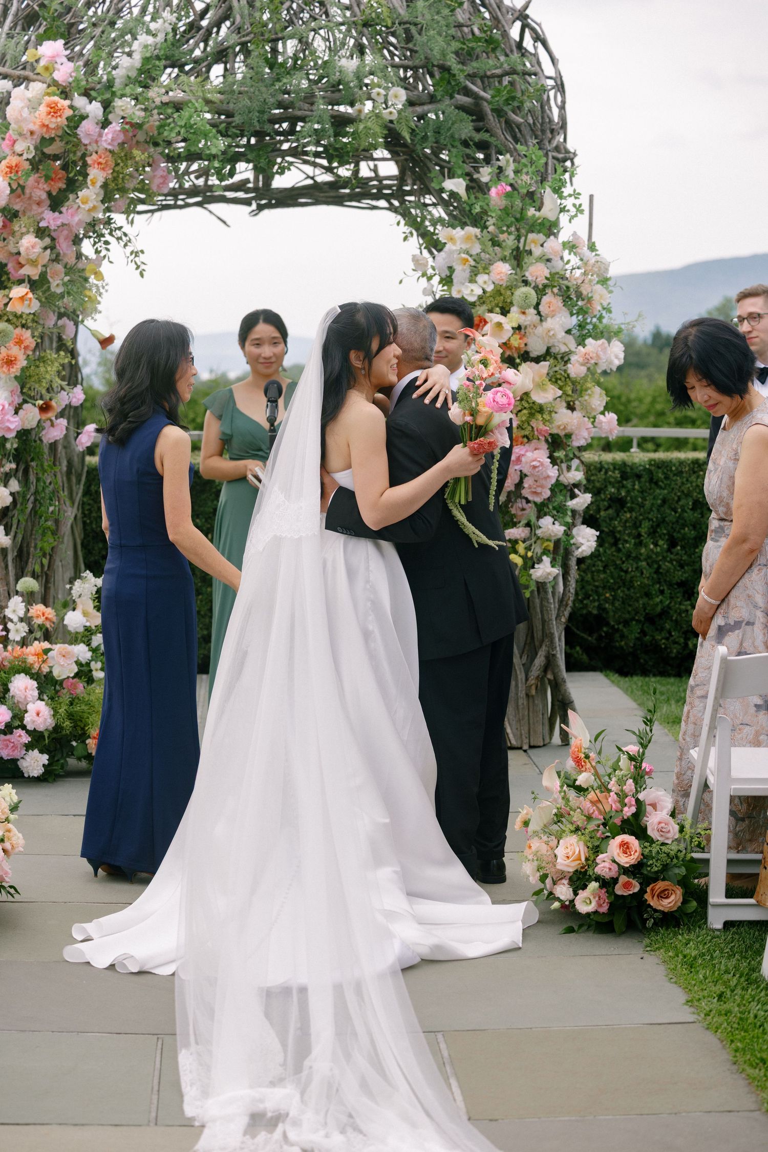 Bride and groom share first kiss under floral arch with pink and peach blooms at outdoor wedding.