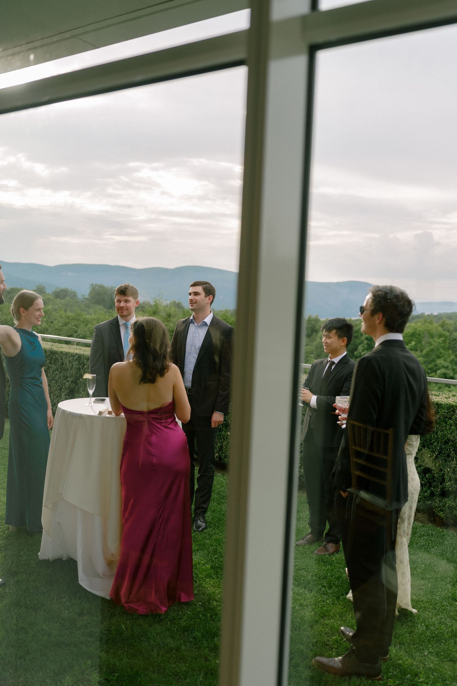 Elegant wedding cocktail hour on an outdoor terrace with mountain views, guests mingling in formal attire.