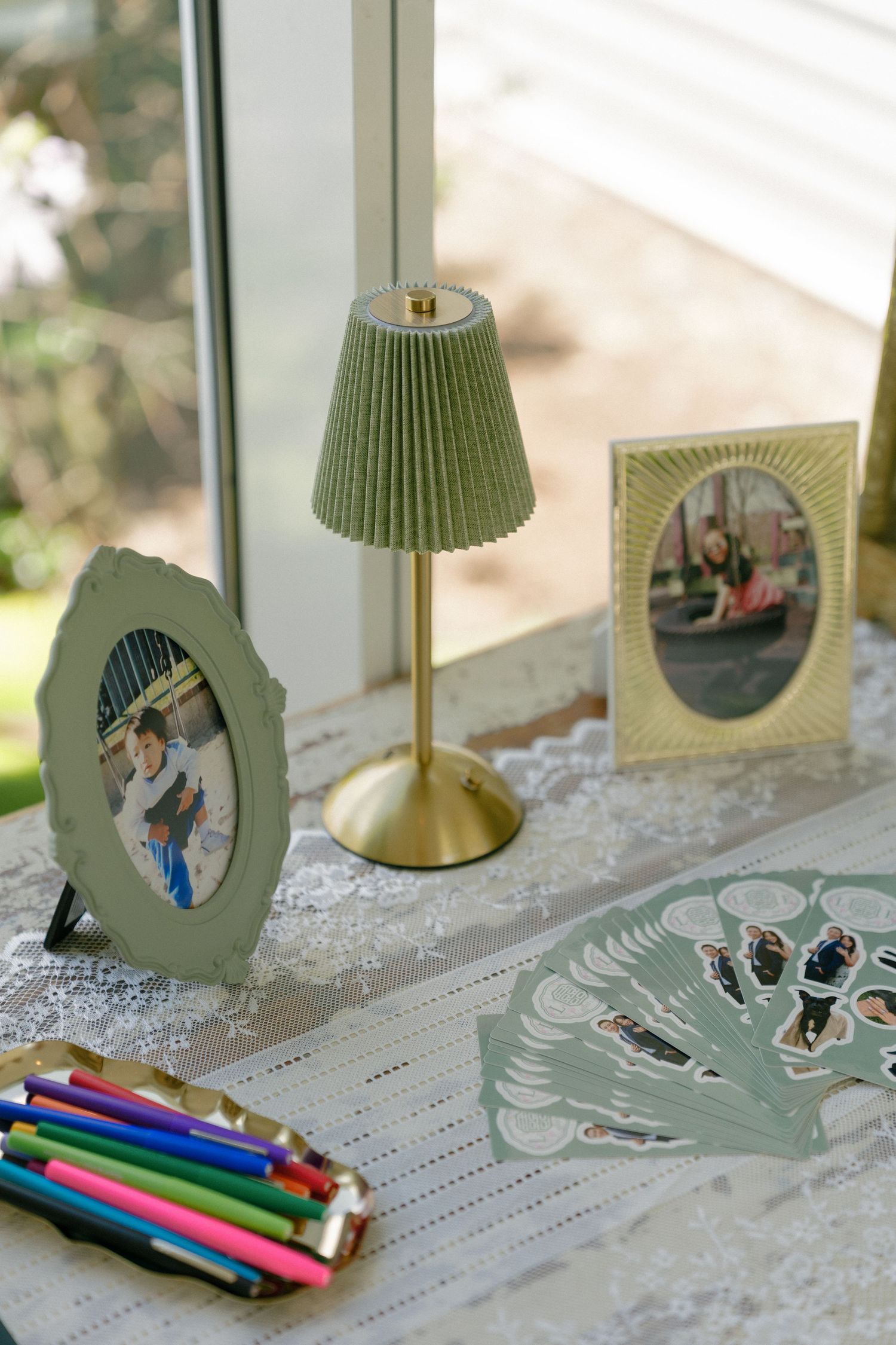 Wedding guest book table with sage green lamp, colored pencils, photo frames, and custom stickers on lace tablecloth.