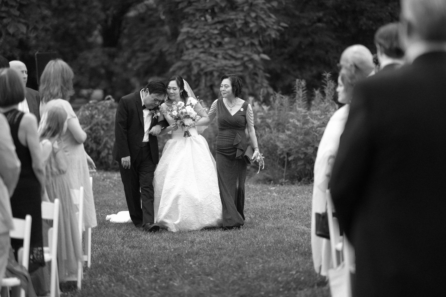 Bride walking down the aisle with family escorts at an outdoor garden wedding ceremony.