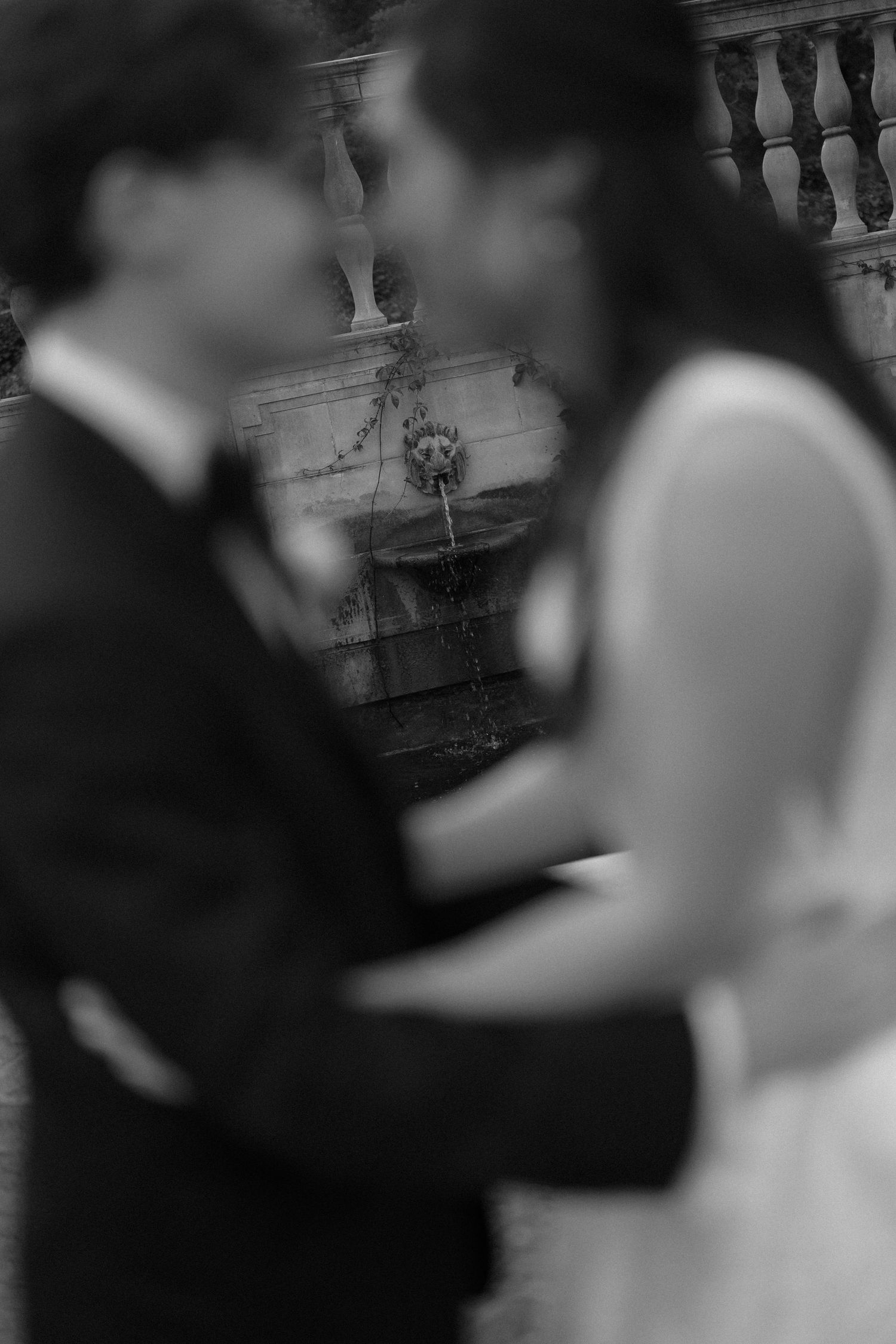 Artistic blurred black and white portrait of bride and groom embracing near a stone fountain.