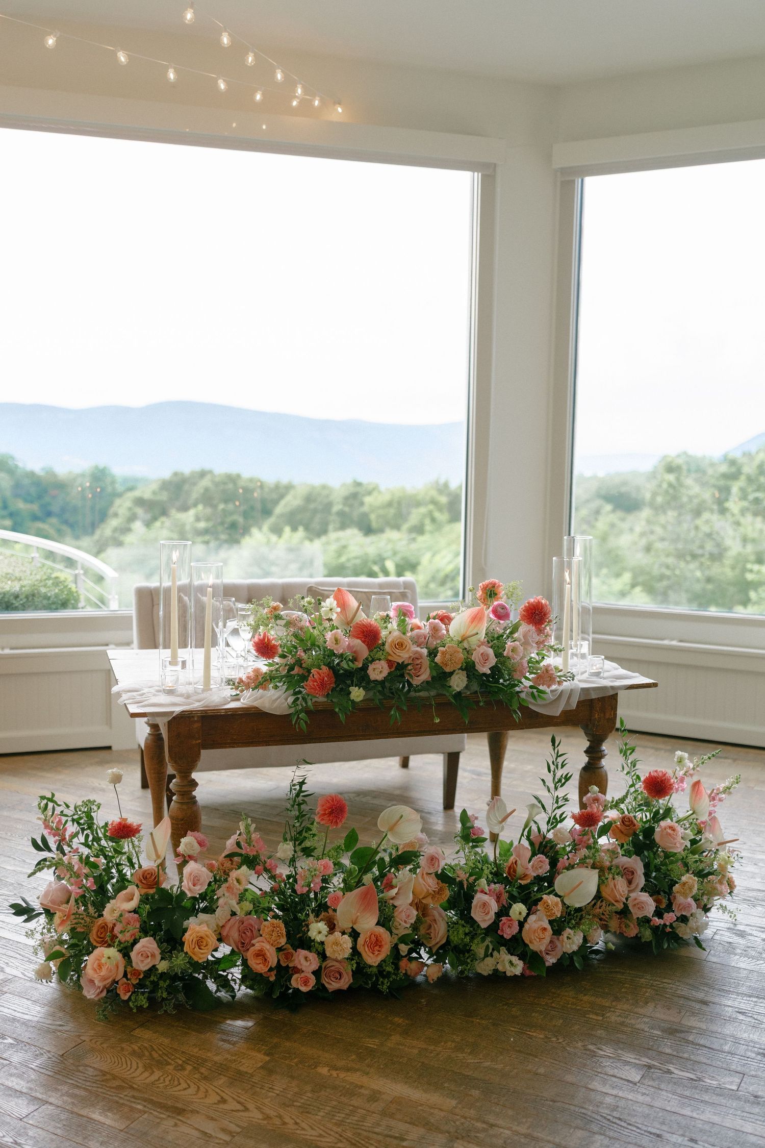 Sweetheart table adorned with lush pink and peach floral arrangements overlooking mountain views.