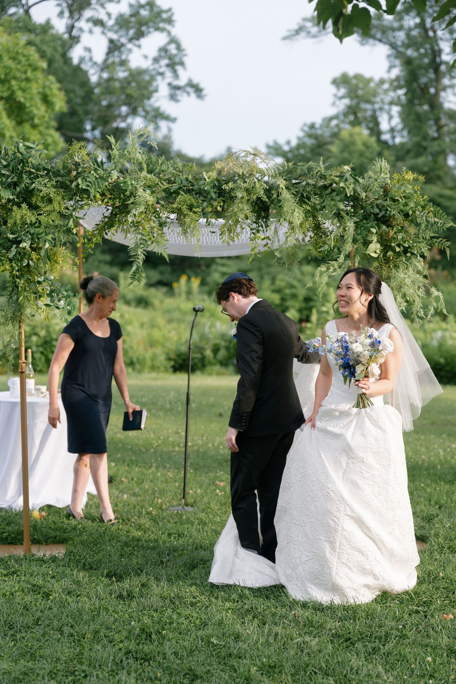 Bride and groom exchange vows under lush greenery chuppah at outdoor Jewish wedding ceremony.