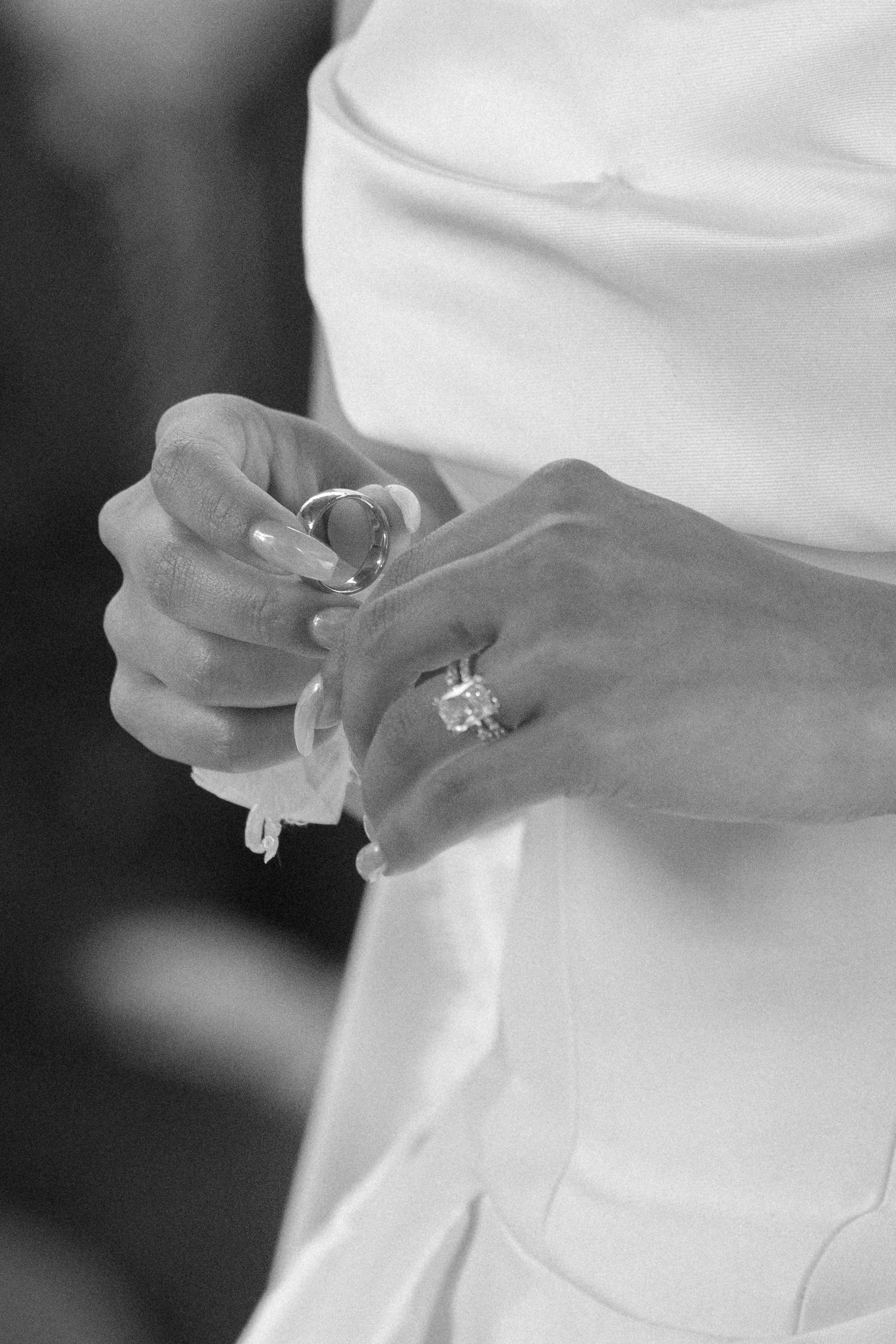 Black and white photo of a bride in white dress showcasing a large diamond engagement ring on her finger.