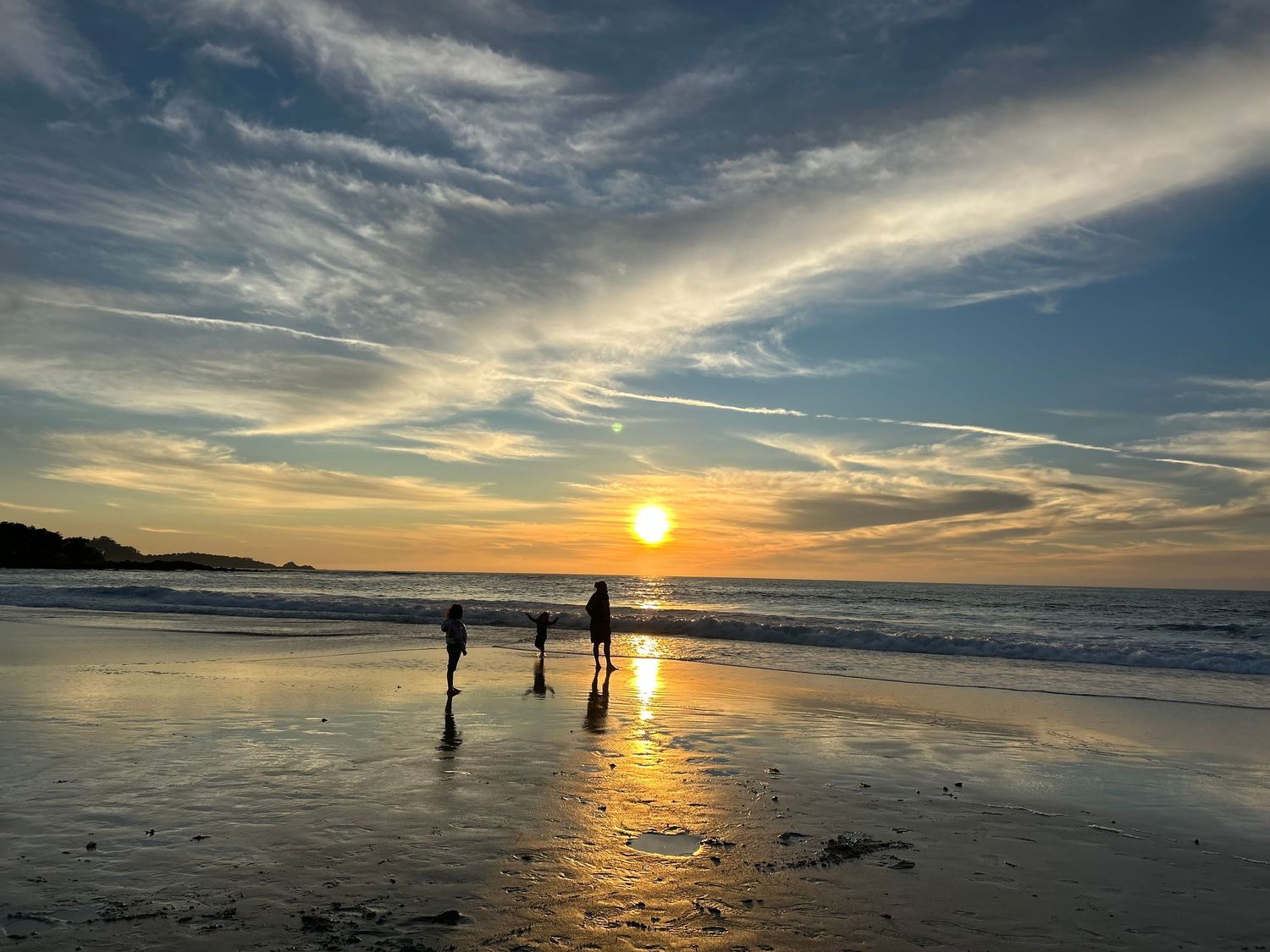 Dramatic sunset over a beach with silhouettes of people walking along the shoreline at low tide.