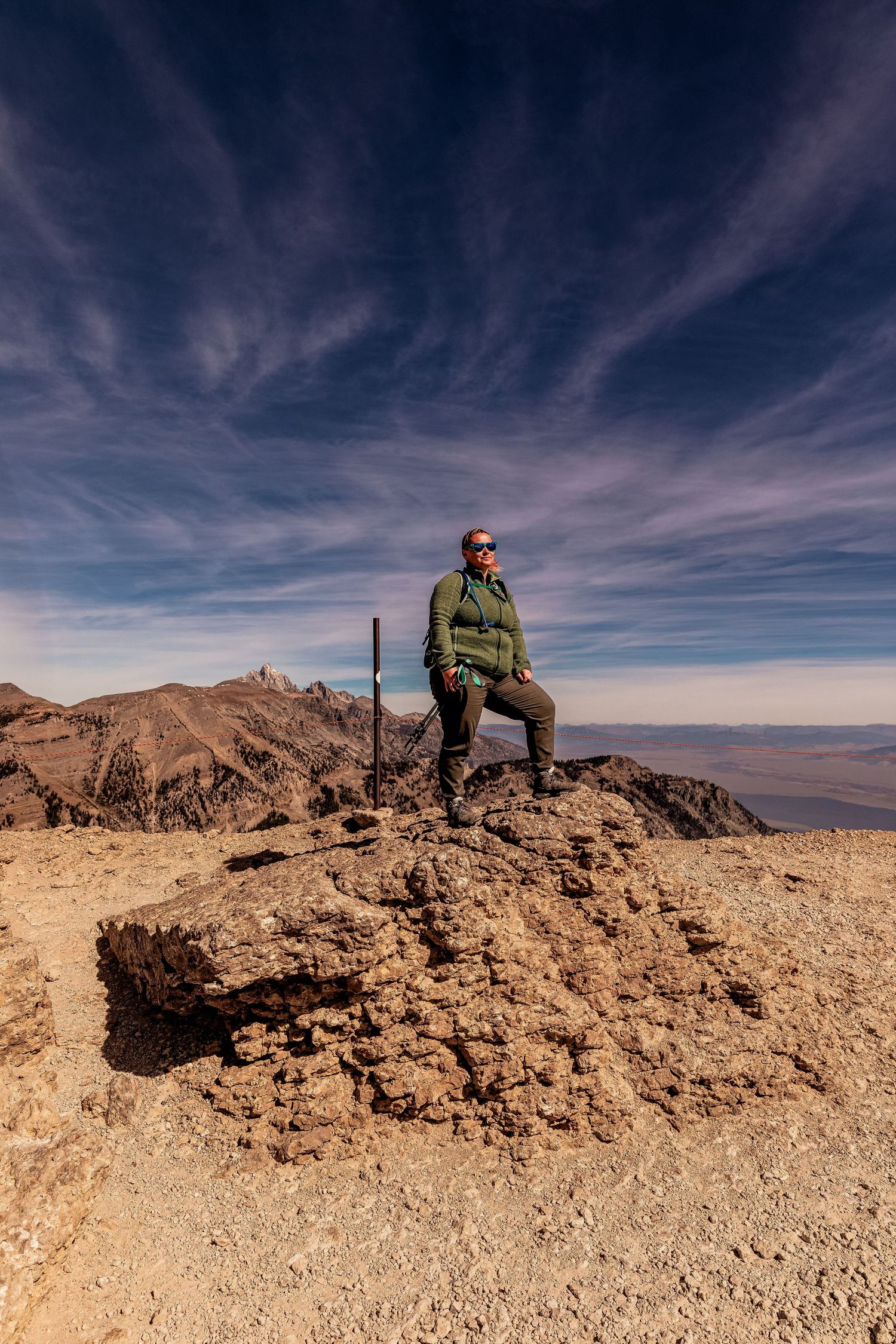 A series of panoramic photos showing a hiker resting atop a rocky desert mountain summit against a dramatic cloudy sky.
